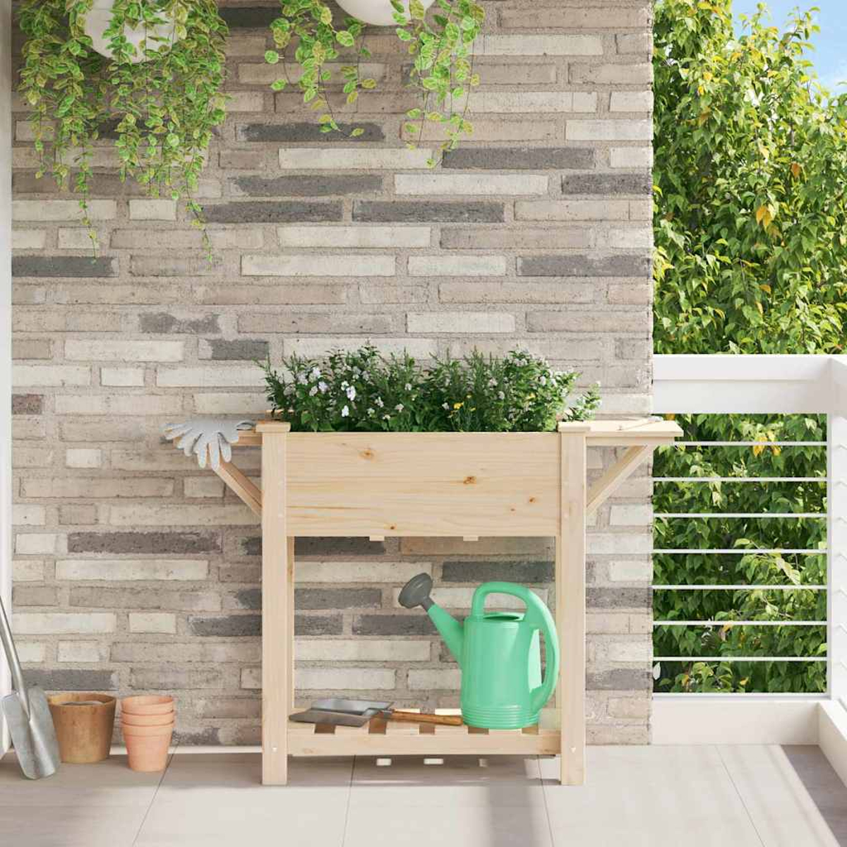 Fioriera in legno su un balcone con piante, annaffiatoio e attrezzi. Muro di mattoni sullo sfondo. Il verde pende dall'alto e cresce all'esterno.