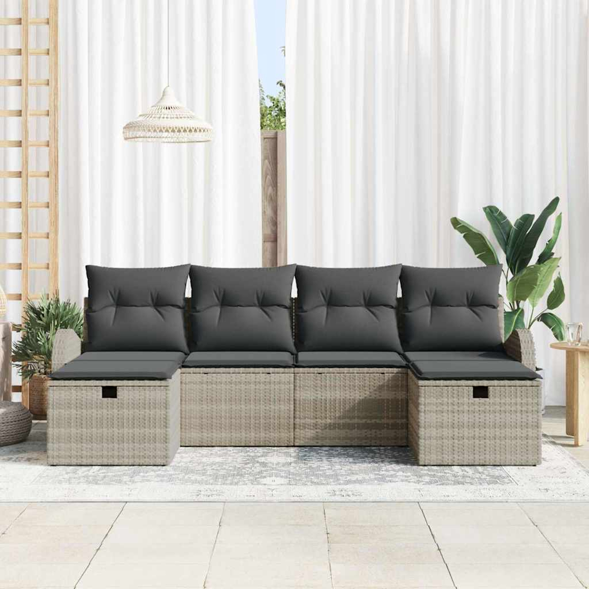 Ein Rattansofa mit grauen Kissen steht auf einem Teppich. Weiße Vorhänge und eine Hängelampe sind im Hintergrund. Pflanzen sind an den Seiten.