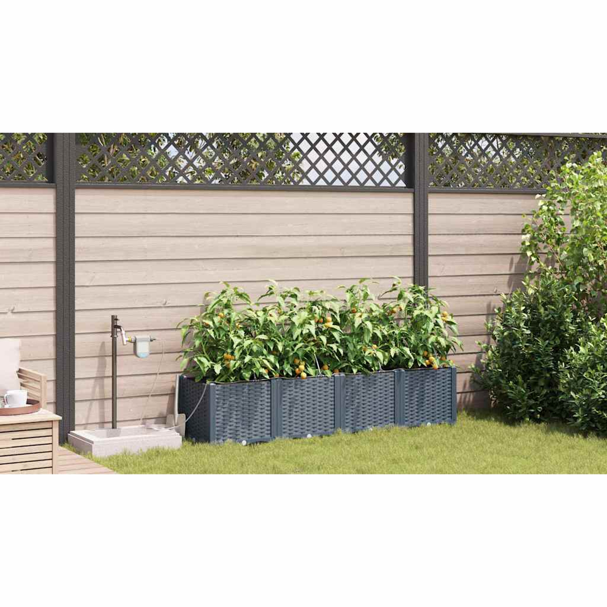 Un giardino con una recinzione in legno, fioriere con piante e un piccolo sistema di irrigazione. Erba verde e piante lussureggianti sullo sfondo.