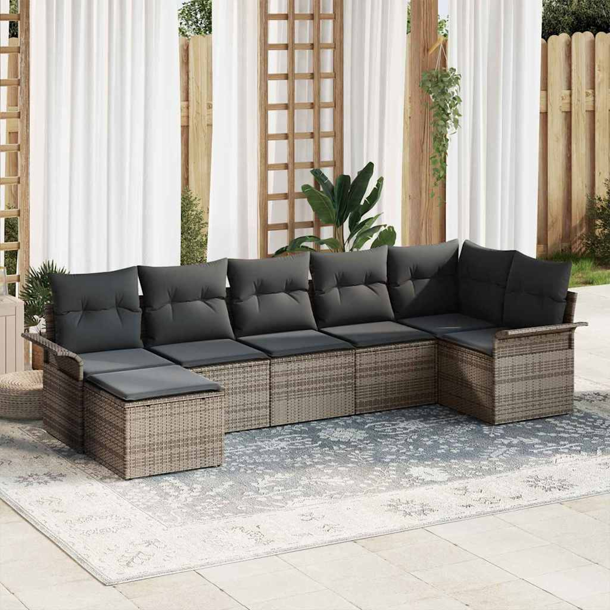 Outdoor-Ecksofa mit grauen Kissen auf einem gemusterten Teppich. Weiße Vorhänge und Holzzaun sind im Hintergrund.