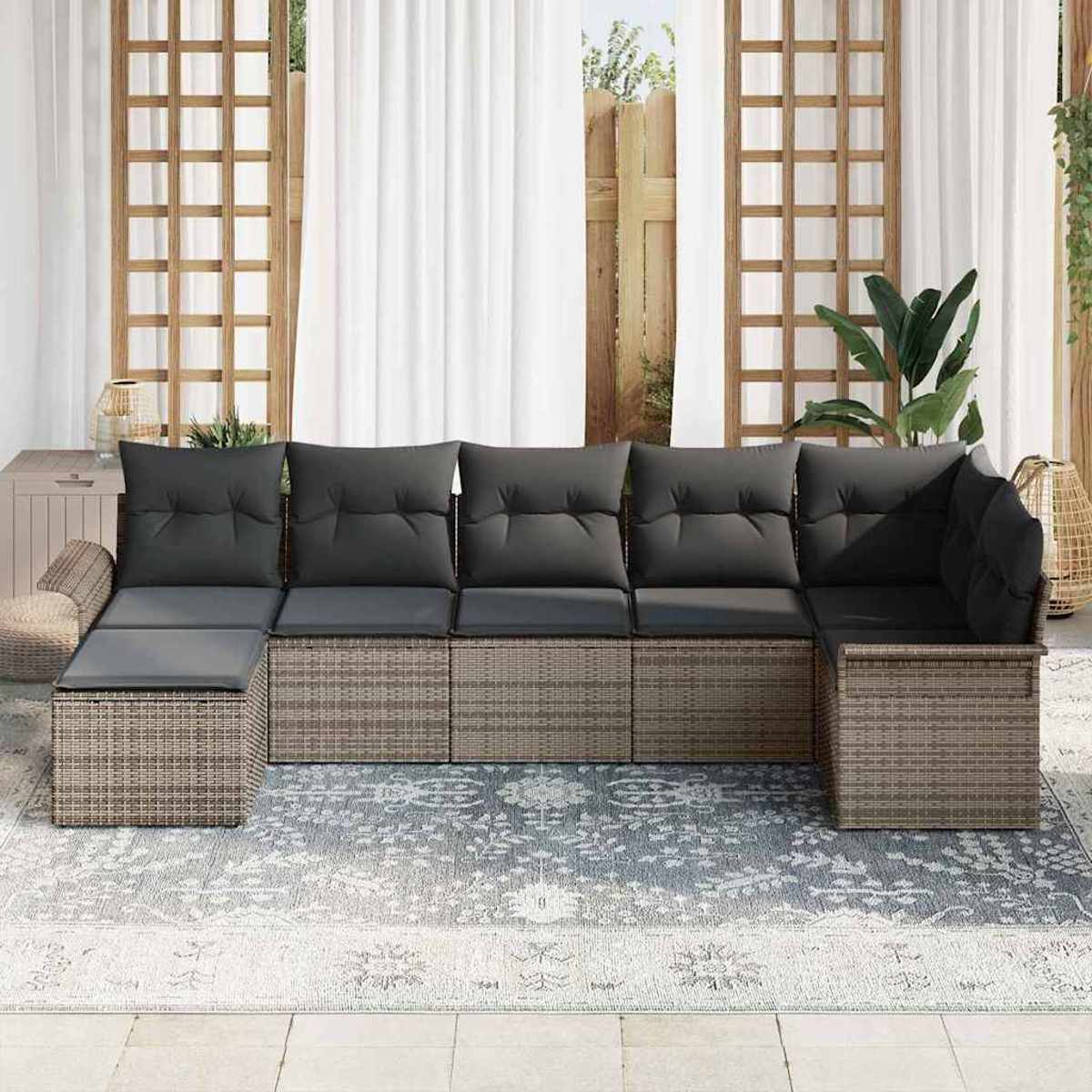 Ein Ecksofa im Freien mit grauen Kissen. Das Sofa steht auf einem gemusterten Teppich, mit weißem Vorhang und Pflanzen.
