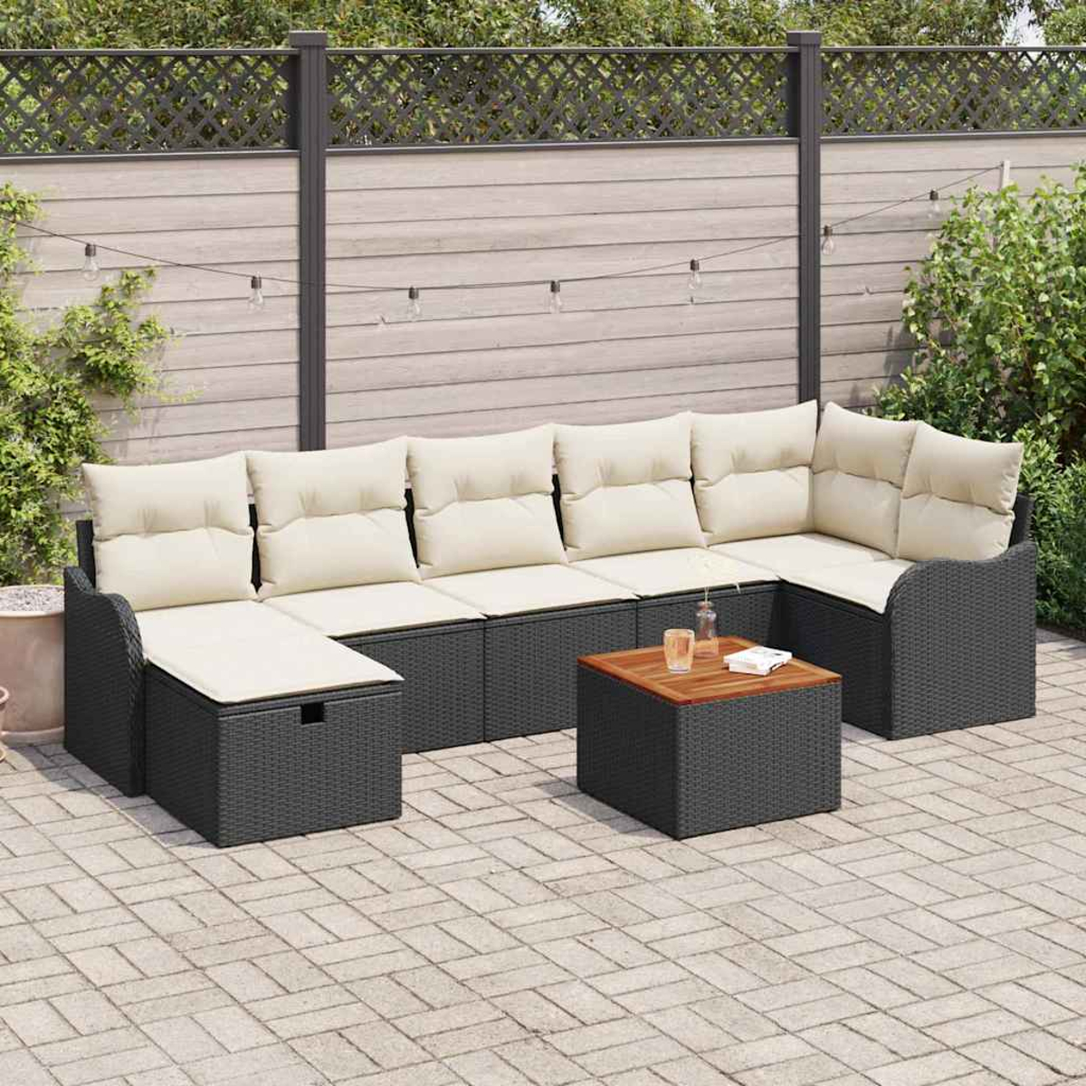 Outdoor-Ecksofa mit beigen Kissen und einem Holztisch. Im Hintergrund ein Zaun, Pflanzen und Lichterketten.