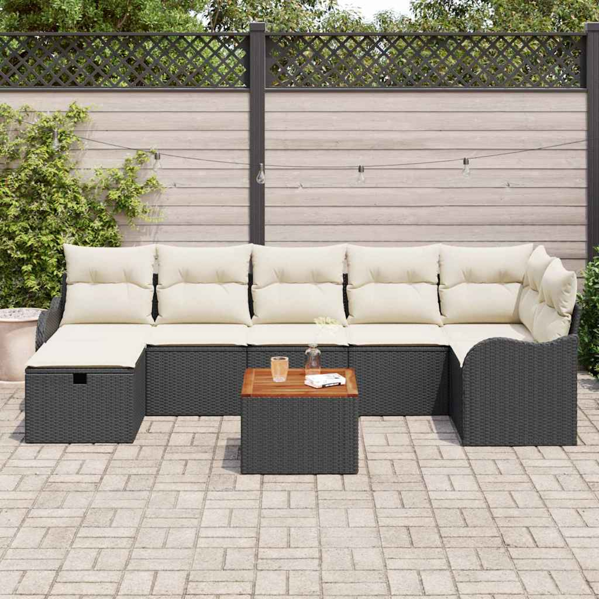 Garten-Sitzgruppe mit cremefarbenen Kissen und grauem Korbgewebe. Ein kleiner Holztisch mit Gläsern und ein Zaun im Hintergrund.
