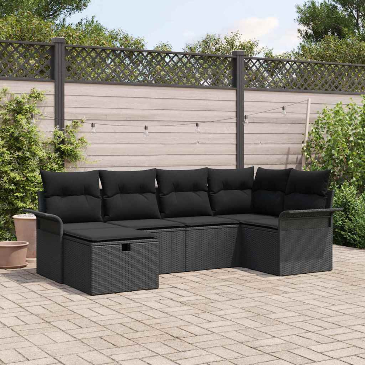 Schwarzes Ecksofa im Freien auf einer Backstein-Terrasse. Im Hintergrund ein Holzzaun und Grün.