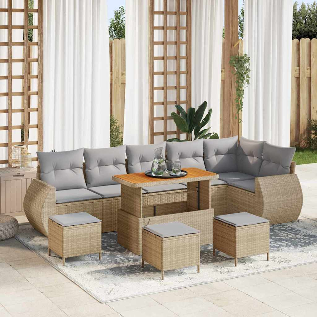 Gartenmöbel-Set aus Korbgeflecht mit grauen Kissen. Enthält ein Ecksofa, einen Couchtisch und Hocker auf einer Terrasse. Weiße Vorhänge im Hintergrund.
