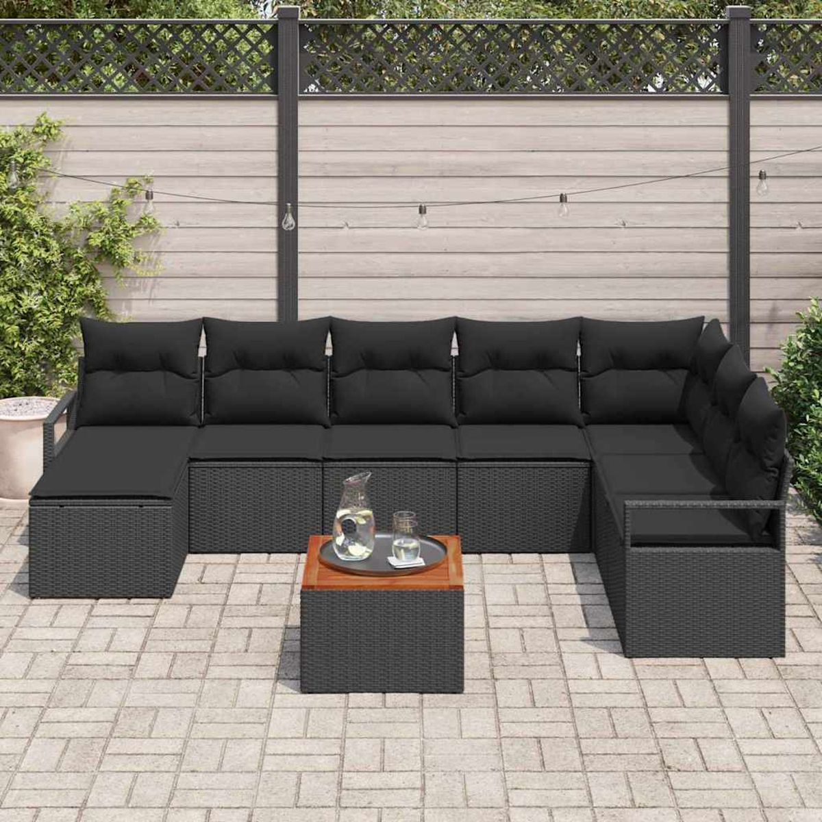 Outdoor-Ecksofa mit schwarzen Kissen und einem kleinen Tisch mit Krug und Gläsern, auf einer Ziegelterrasse.
