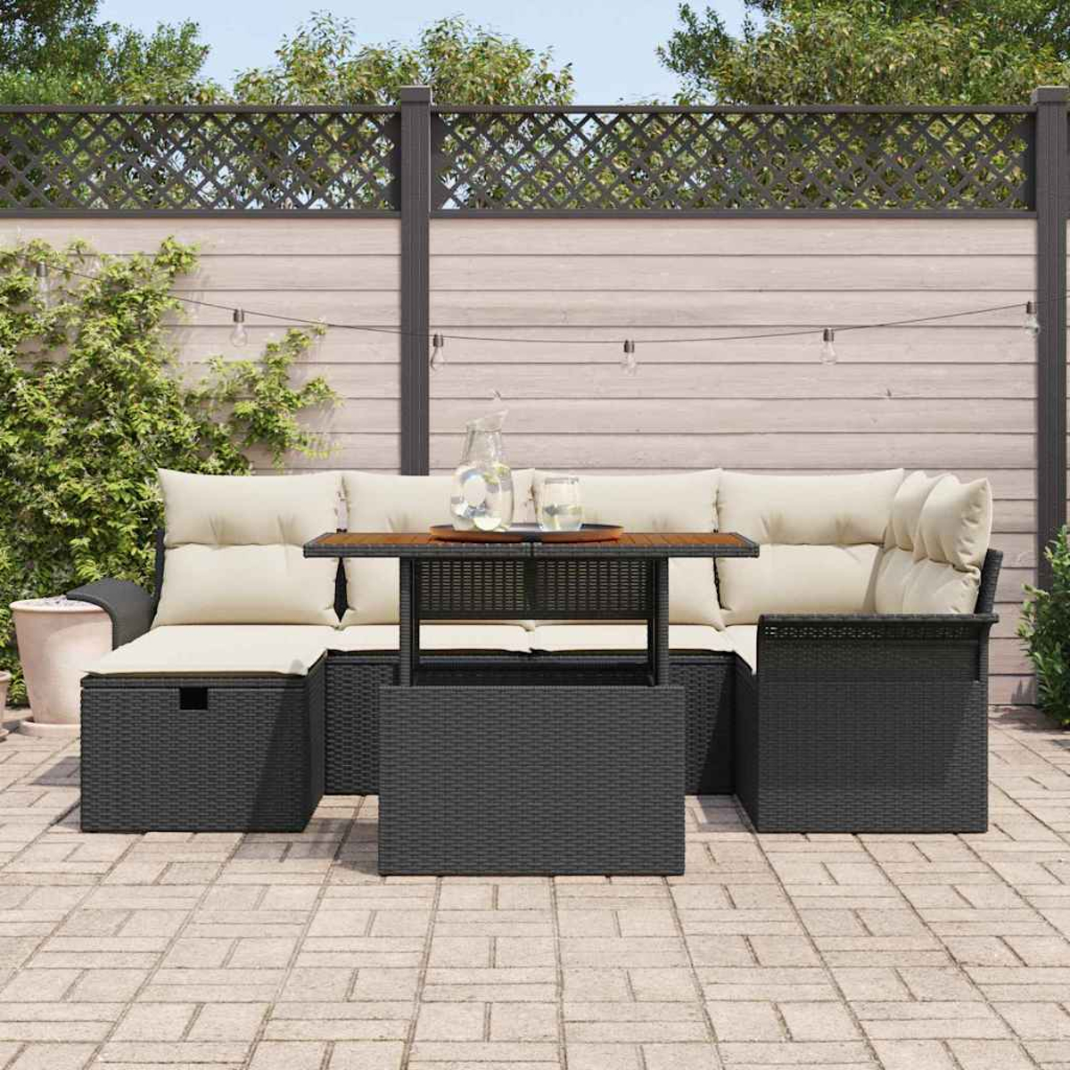 Garten-Terrassenset. Schwarze Korbmöbel mit cremefarbenen Kissen. Holztisch, Glaskrug und Lichterketten. Stein-Terrasse und Holzzaun.
