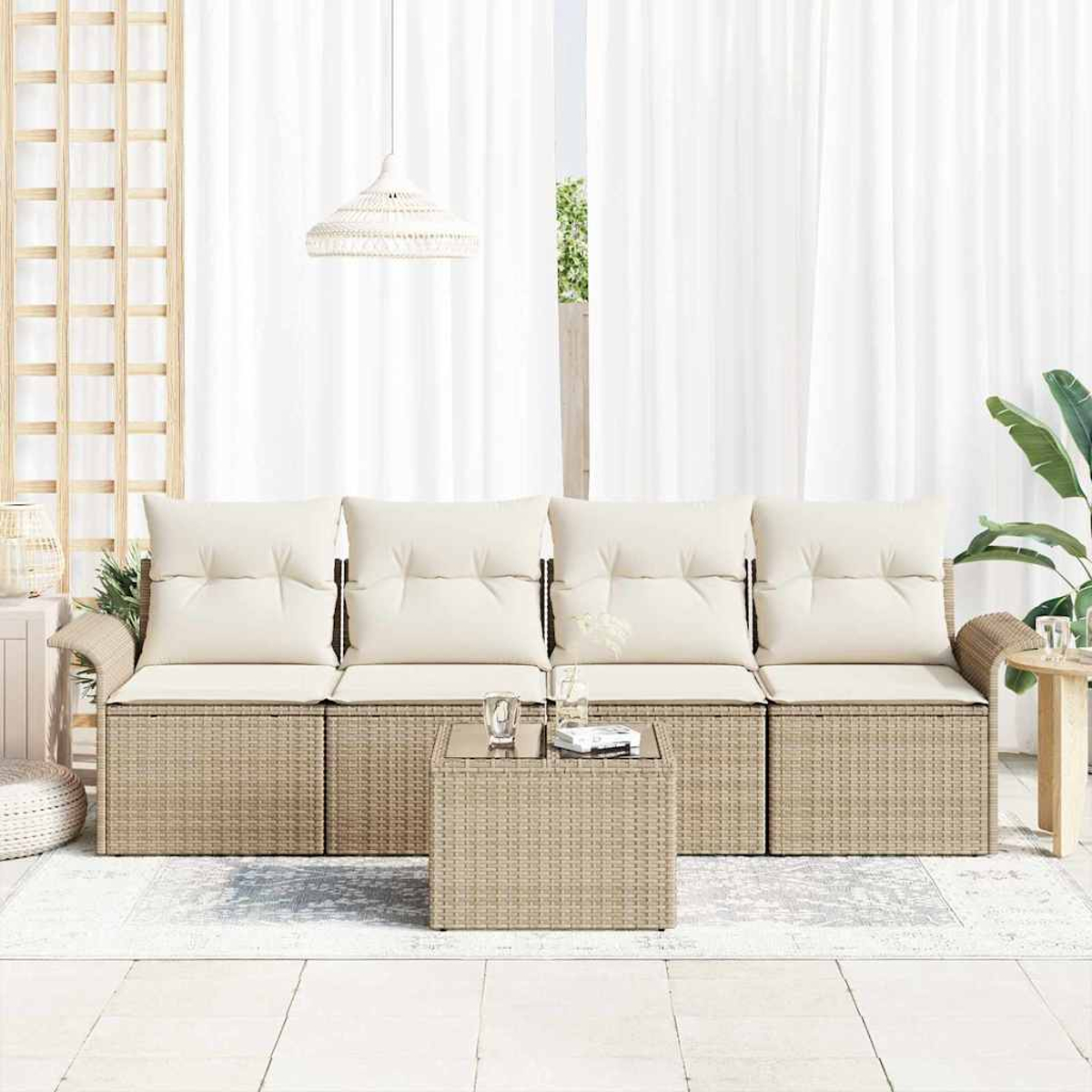 Rattansofa mit cremefarbenen Kissen und einem Tisch mit Glasplatte. Weiße Vorhänge und eine Hängelampe sind im Hintergrund, zusammen mit Pflanzen.