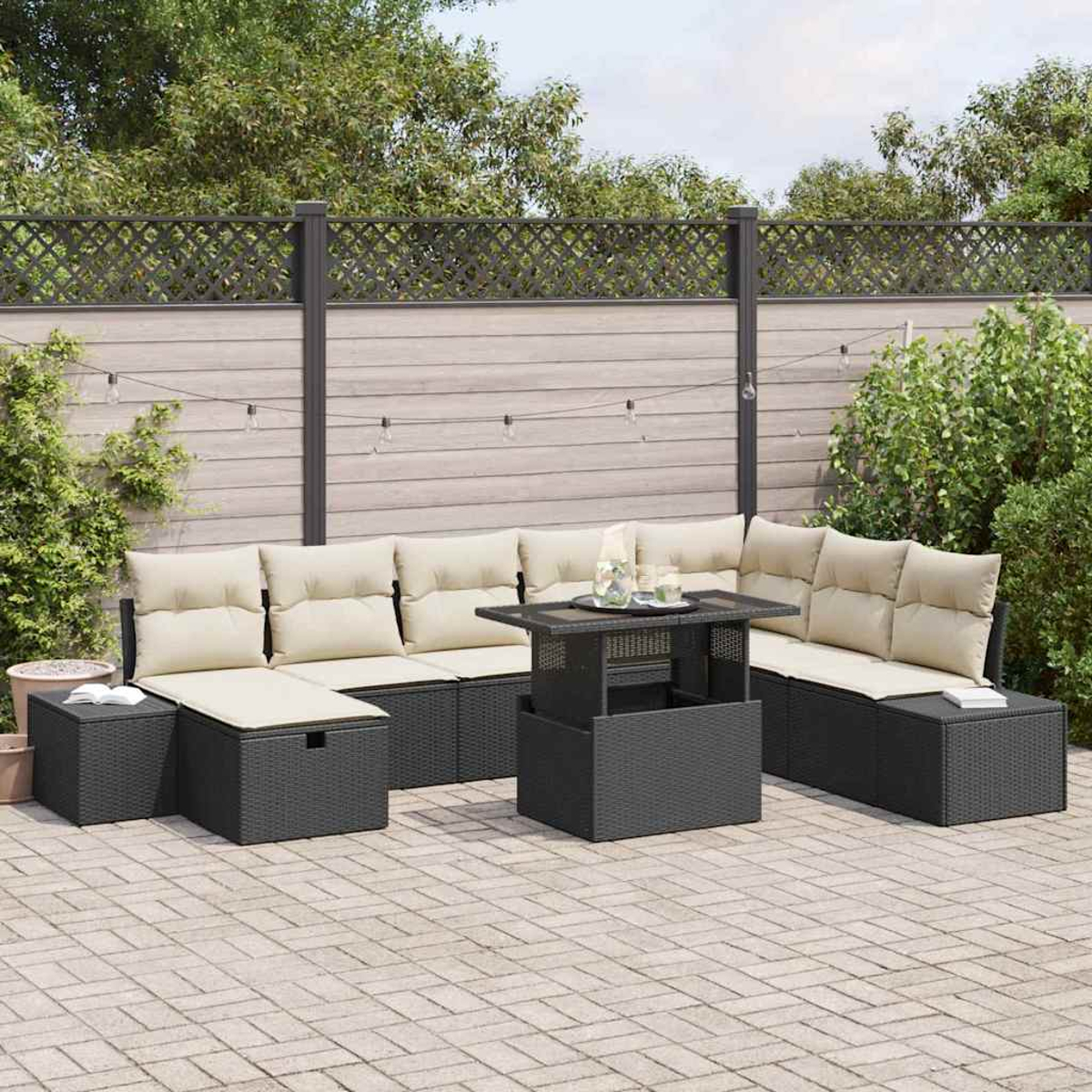 Schwarzes Outdoor-Wicker-Möbelset mit beigen Kissen, Couchtisch und Backstein-Terrasse. Im Hintergrund ein Zaun und Grün.