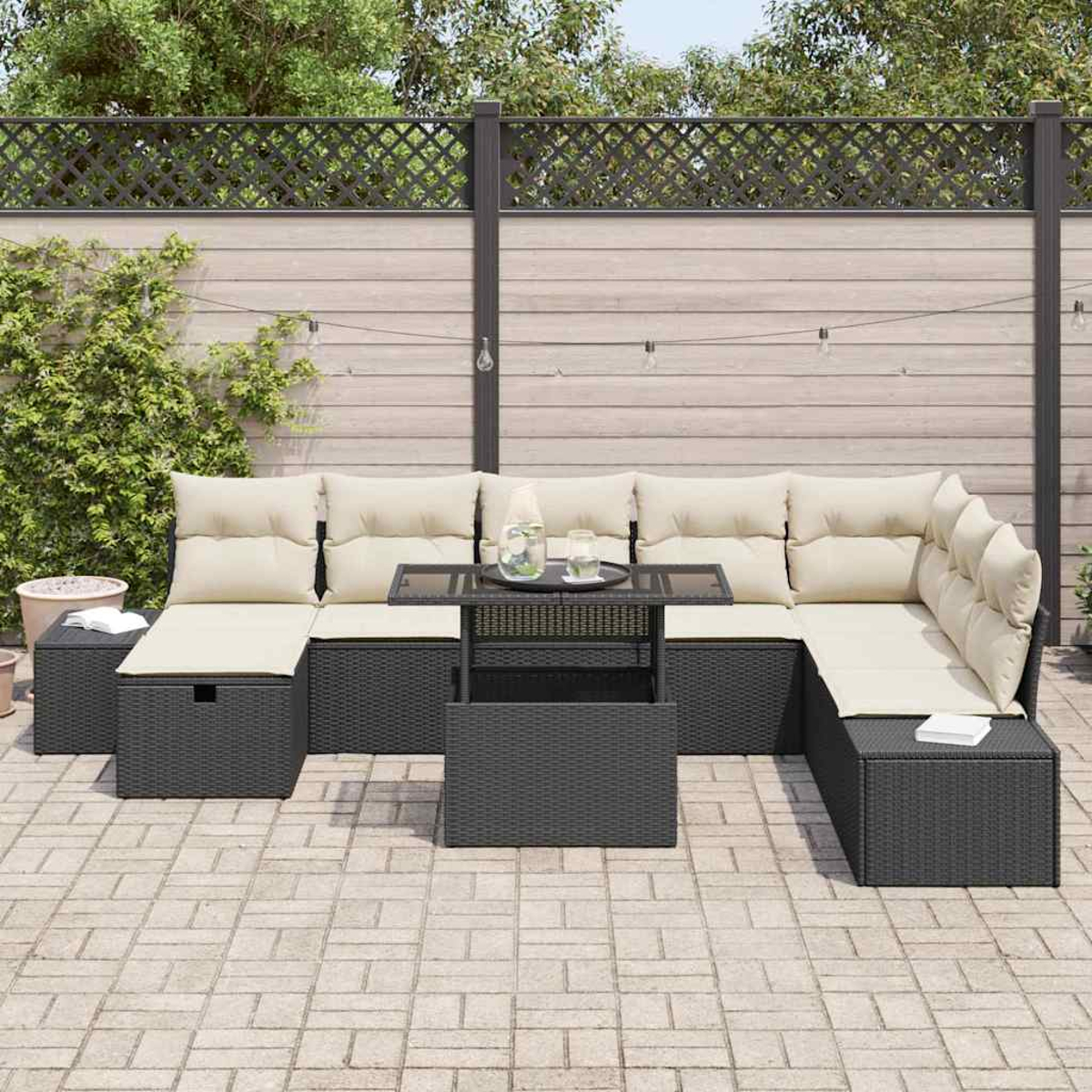 Garten-Terrassenset mit beigefarbenen Kissen, schwarzen Korbmöbeln und einem Tisch mit Glasplatte. Ein Holzzaun und Pflanzen sind im Hintergrund.