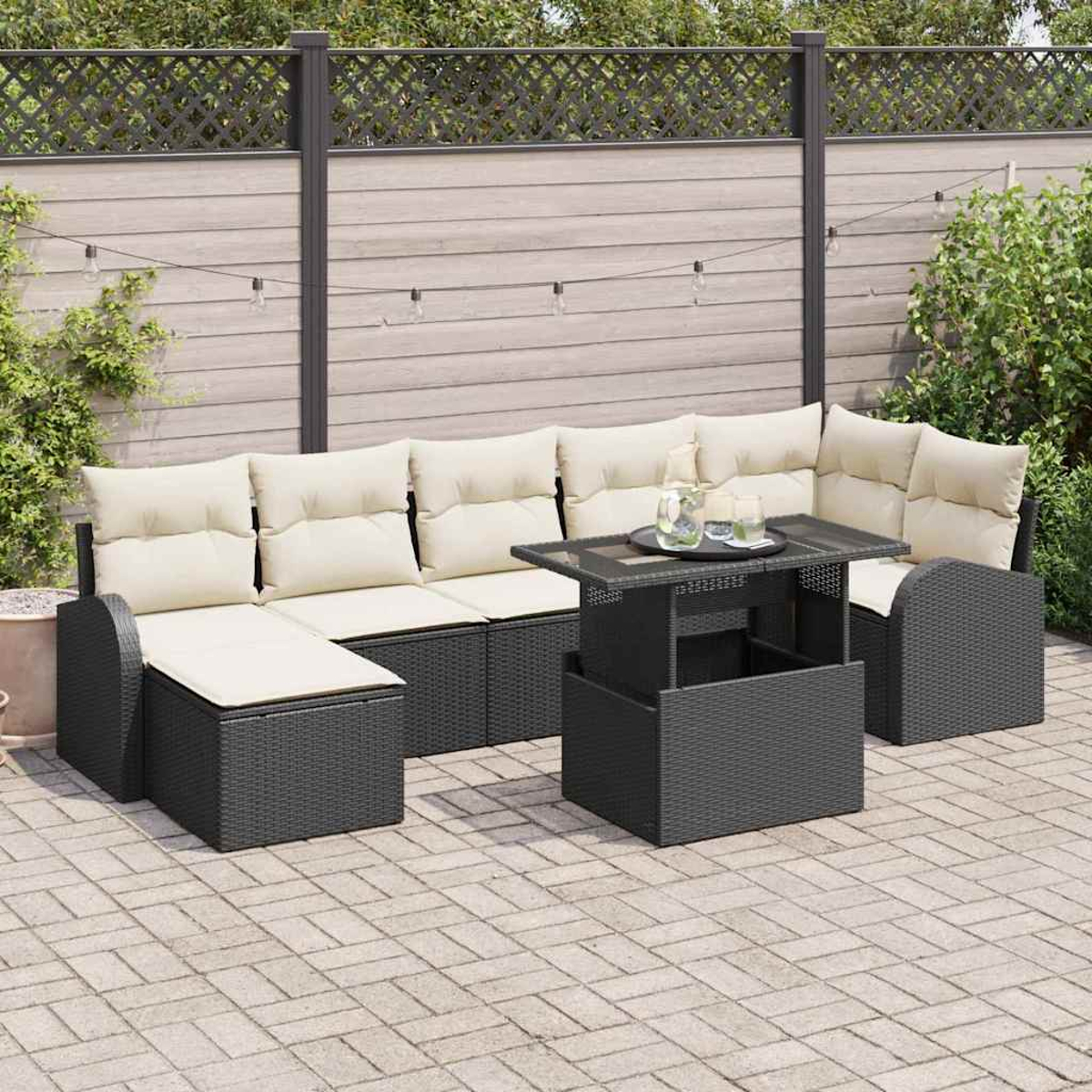 Gartenmöbel-Set mit beigefarbenen Kissen. Enthält Sofa, Tisch und Stühle. Vor Holzzaun und Grün.
