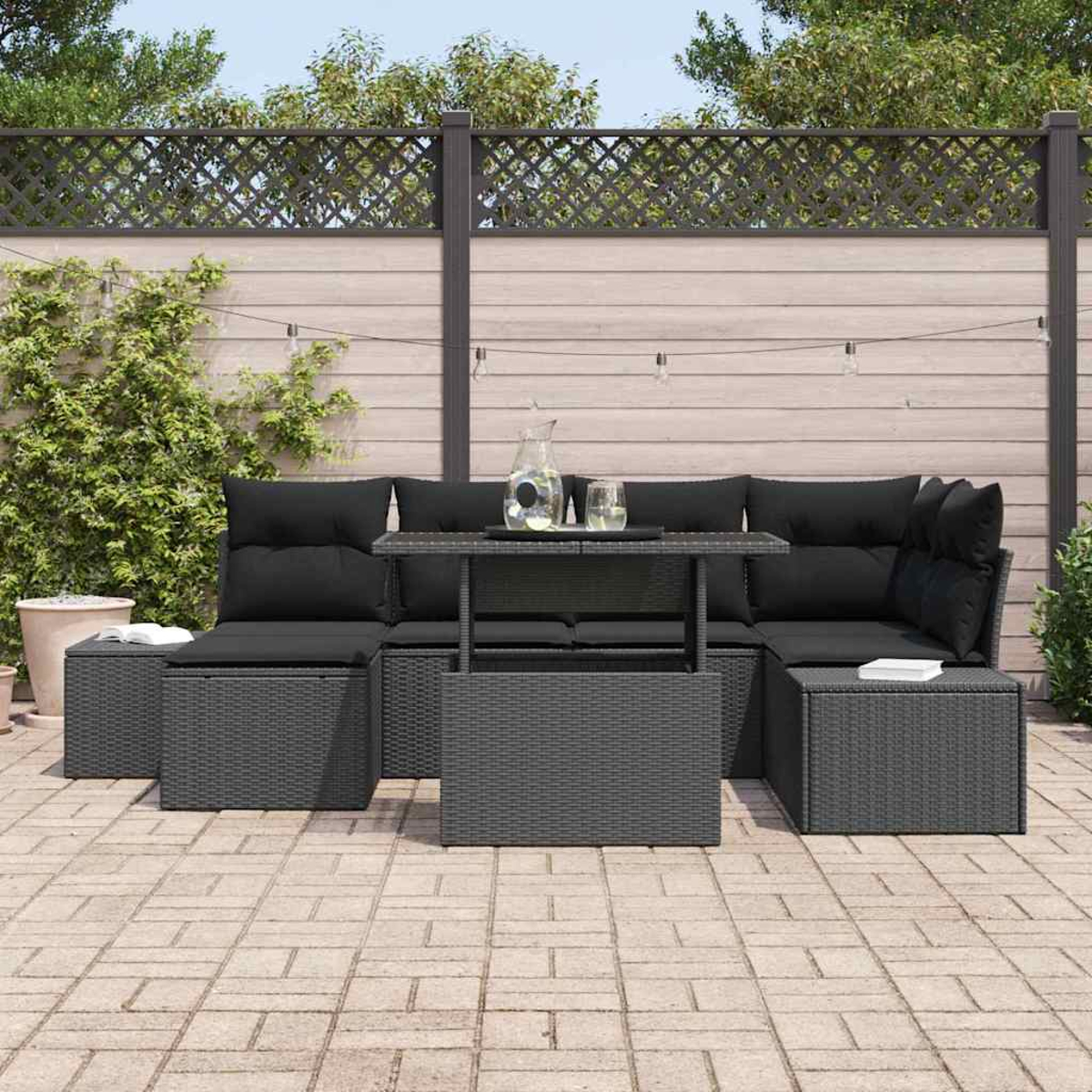 Graues Outdoor-Wicker-Möbelset mit schwarzen Kissen, einem Glastisch und einem Holzzaun im Hintergrund.