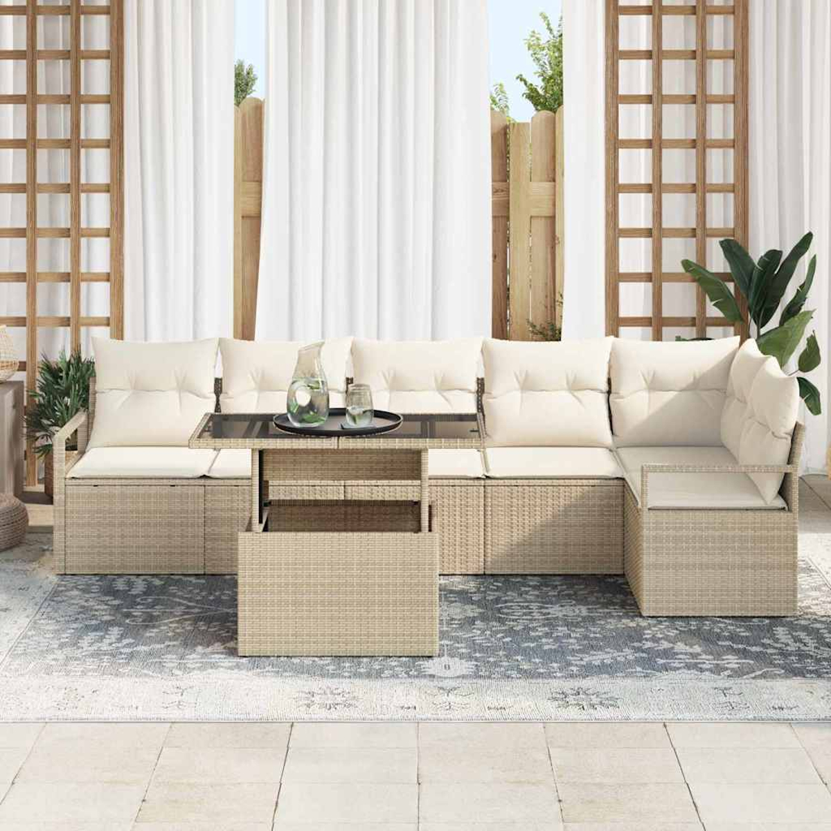 Sofá de ratán exterior con cojines crema y mesa de centro con tapa de cristal. Cortinas blancas y alfombra estampada.