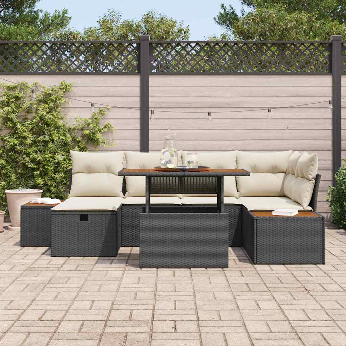 Outdoor-Ecksofa mit beigen Kissen, einem Tisch mit Gläsern und einer Kanne, auf einer Ziegelterrasse. Zaun und Grün im Hintergrund.