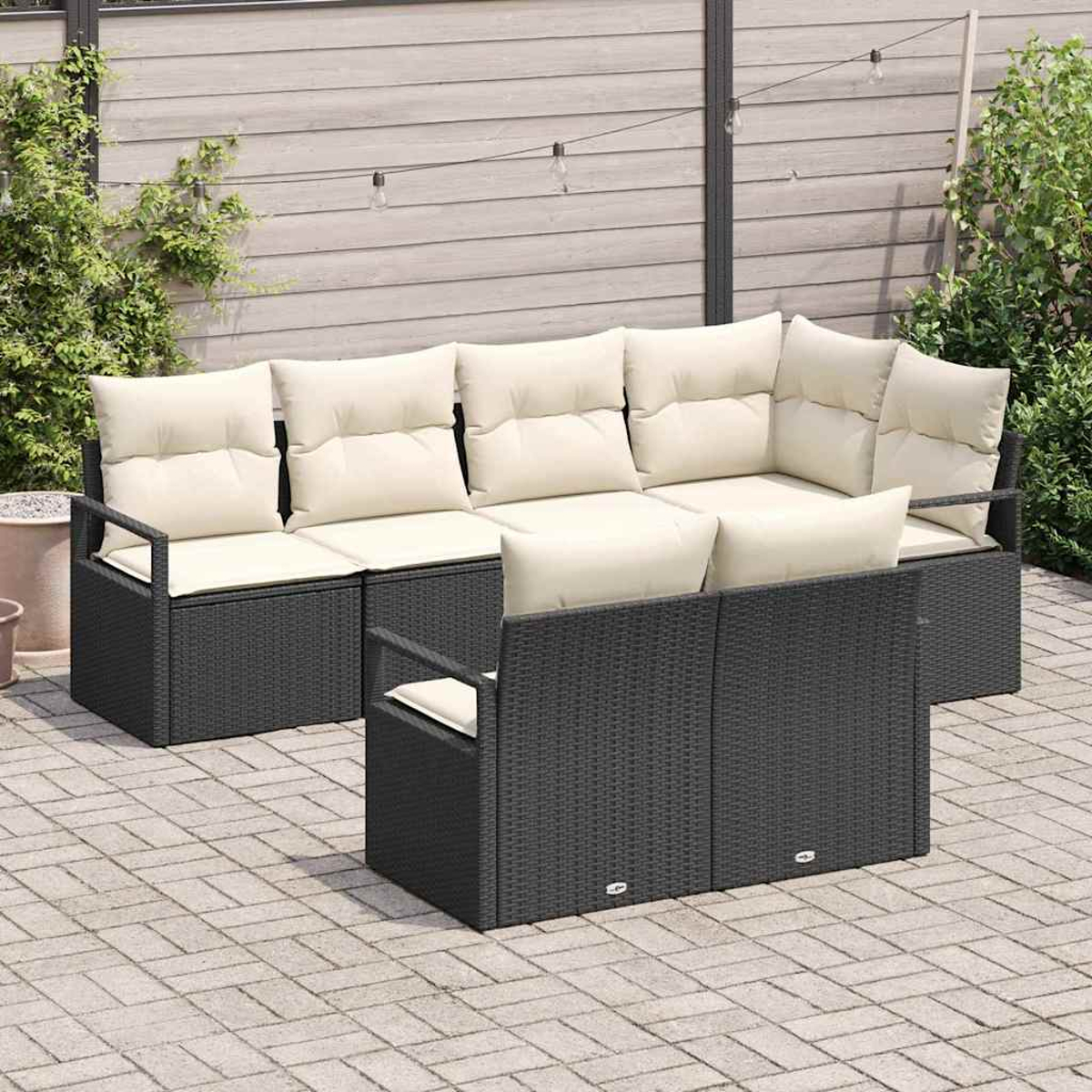 Juego de muebles de patio al aire libre. Sofá de mimbre gris oscuro con cojines crema. Sobre un patio de ladrillos, con vegetación.