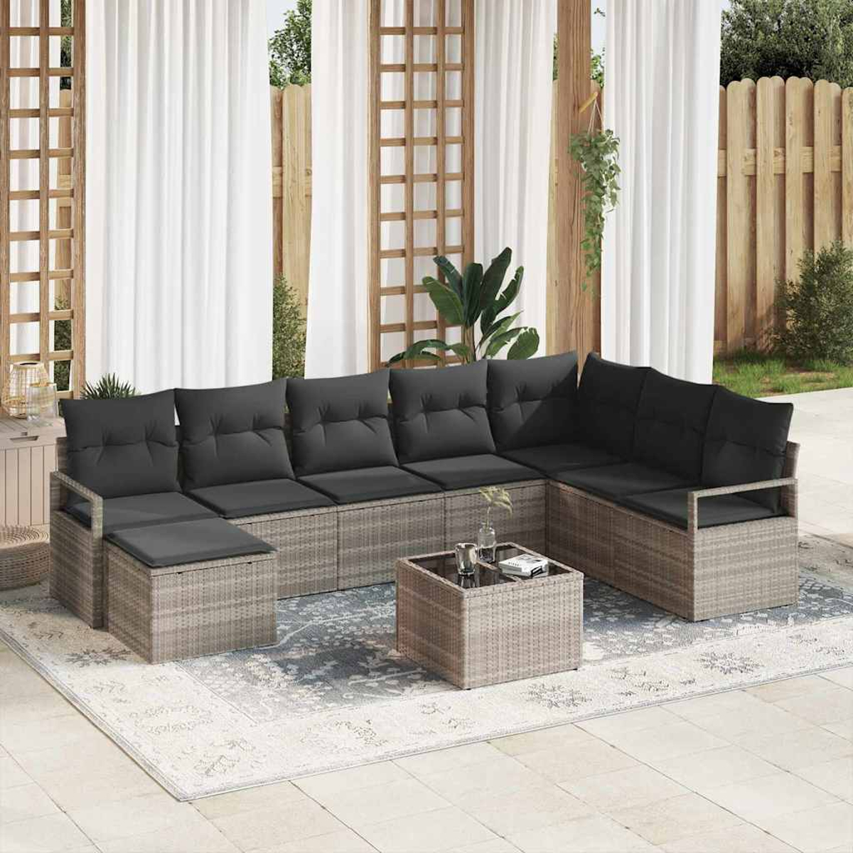 Outdoor-Ecksofa mit dunkelgrauen Kissen, Couchtisch und Teppich. Weiße Vorhänge und Holzzaun im Hintergrund.
