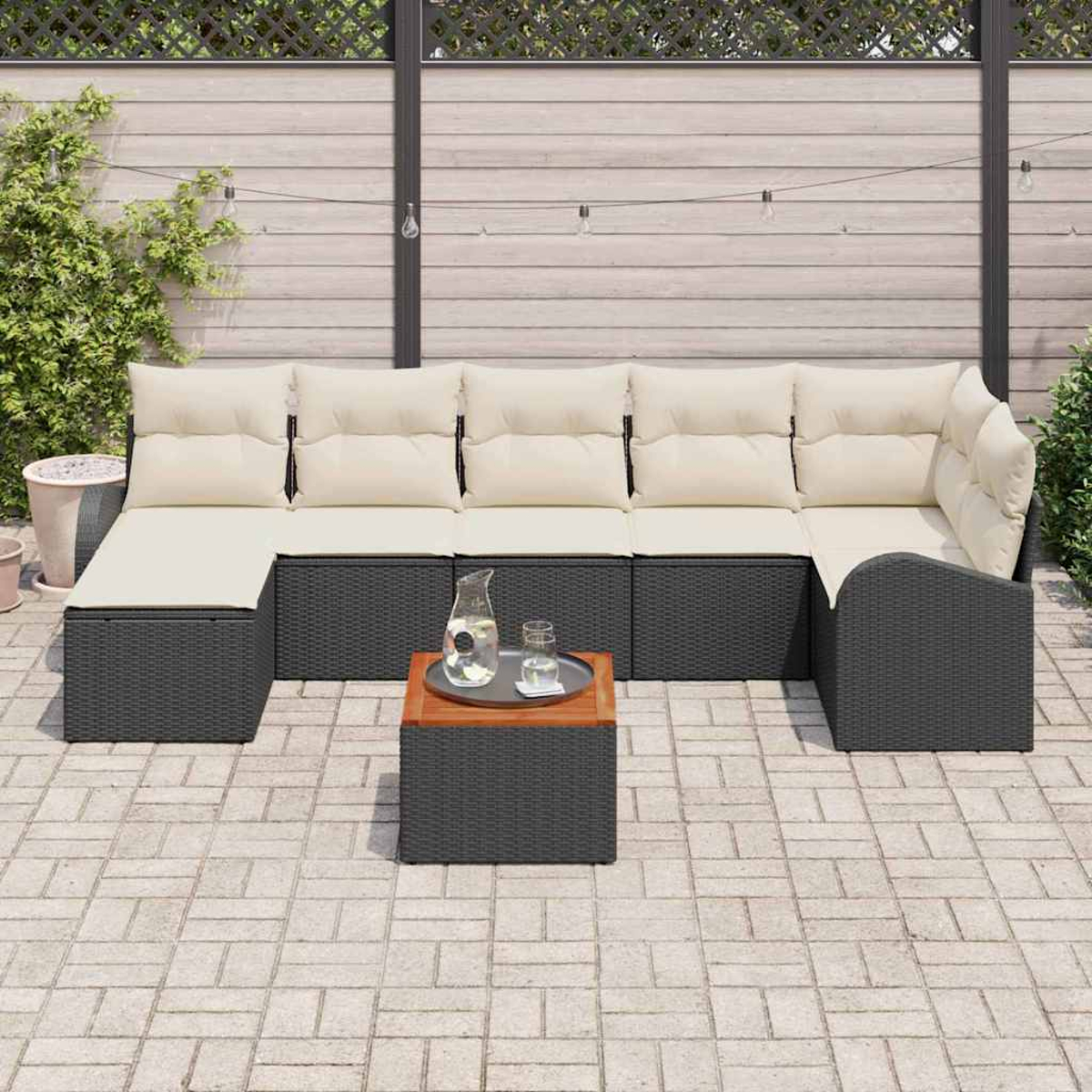 Sofá seccional exterior con cojines crema, mimbre negro. Una mesa cuadrada de madera tiene una jarra y un vaso en el patio.