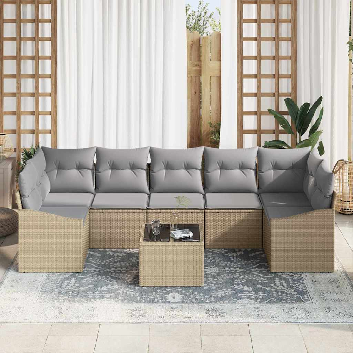 Outdoor-Ecksofa mit grauen Kissen und kleinem Tisch auf einem gemusterten Teppich. Im Hintergrund weiße Vorhänge und Holzgitter.
