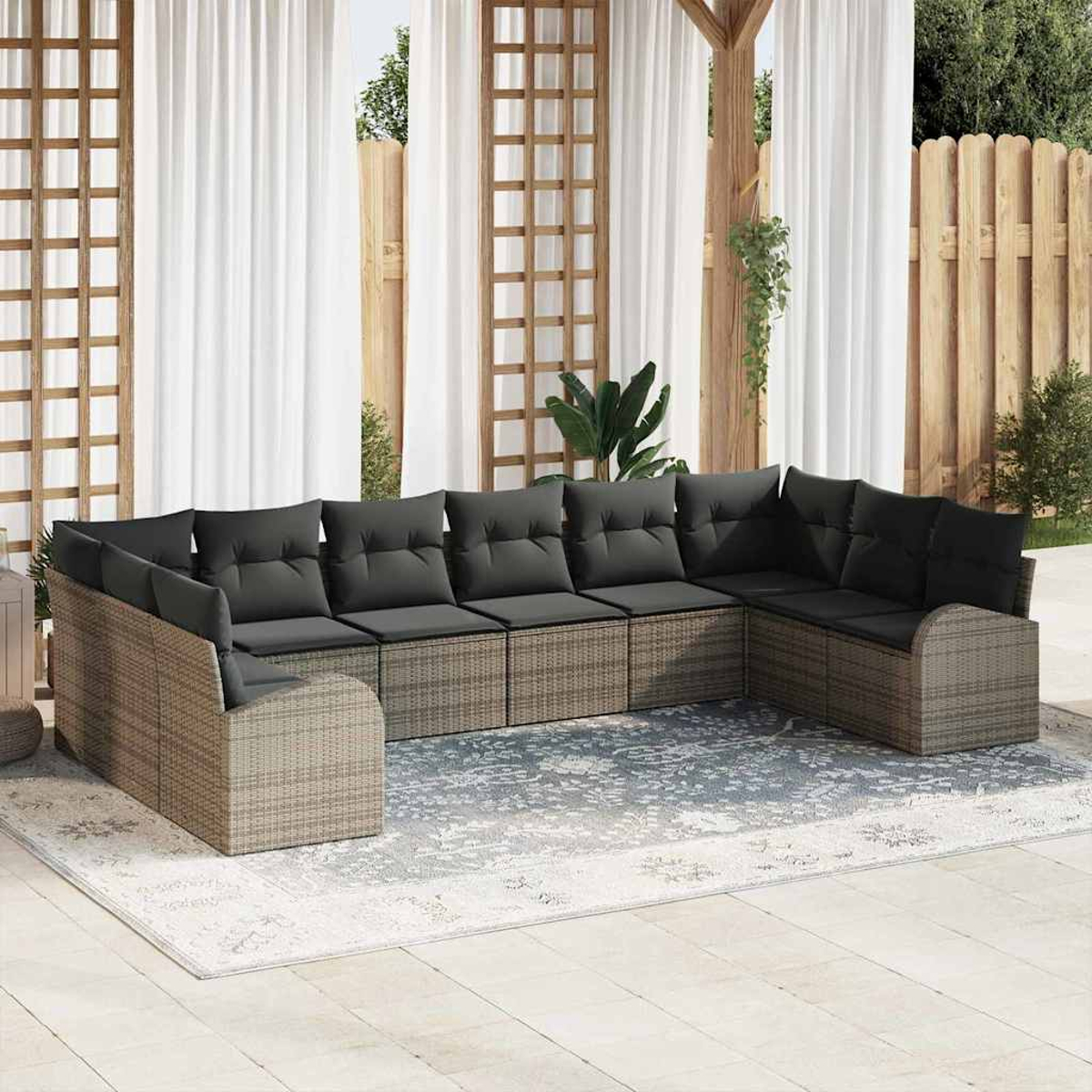 Ein großes Ecksofa mit grauen Kissen im Freien steht auf einem Teppich. Weiße Vorhänge und ein Holzzaun sind im Hintergrund.