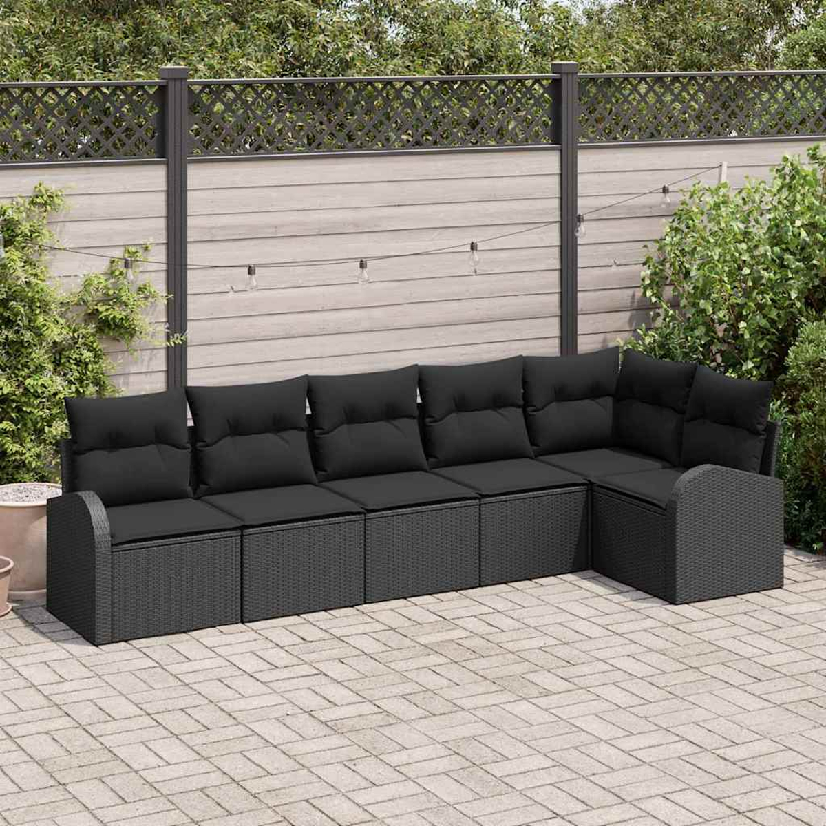 Outdoor-Ecksofa mit schwarzen Kissen und einem korbähnlichen Untergestell auf einer Ziegelterrasse. Ein Holzzaun mit Pflanzen im Hintergrund.