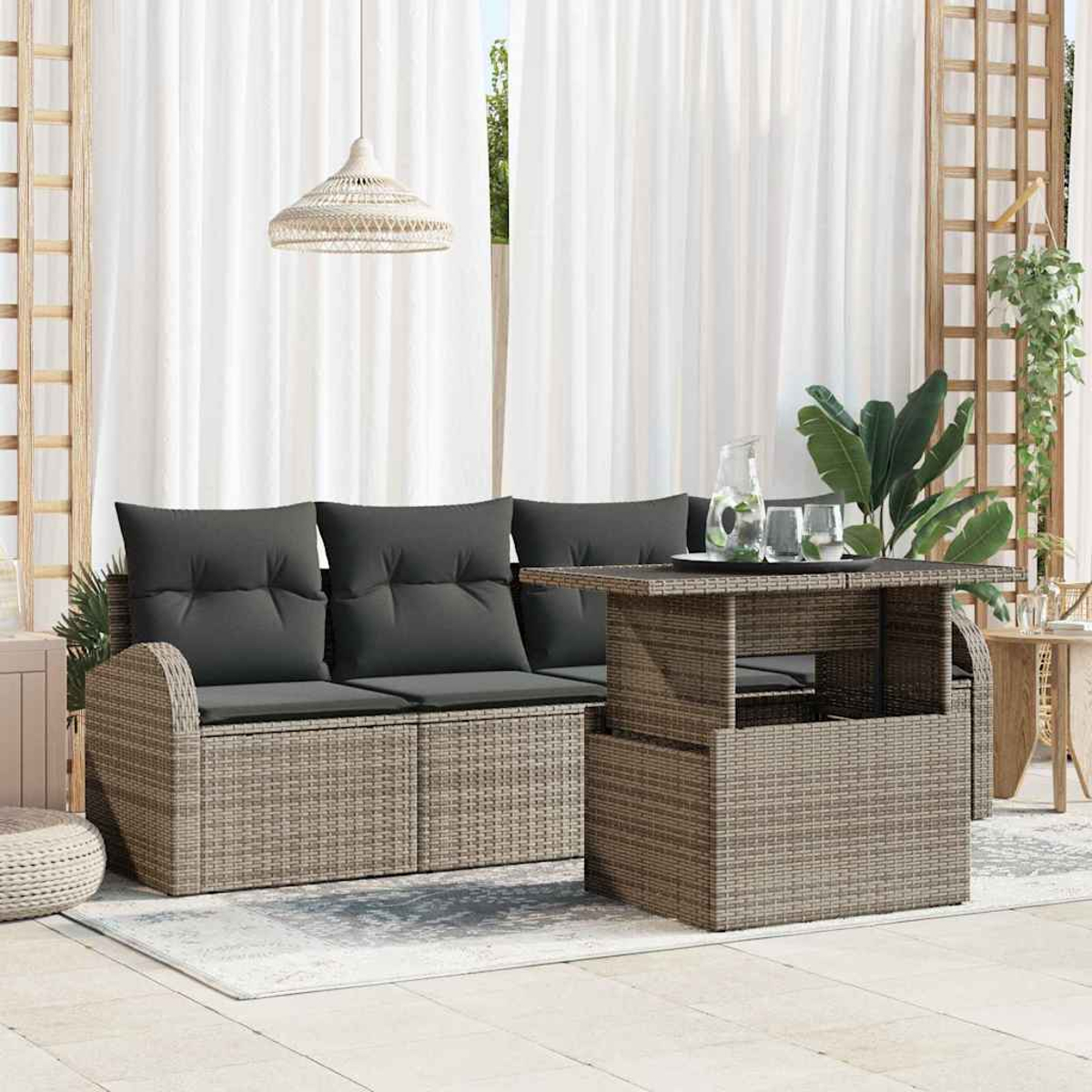 Terrassengarnitur mit Sofa, Tisch und Pflanzen. Graue Kissen, Rattanmöbel, weiße Vorhänge und eine Hängeleuchte.