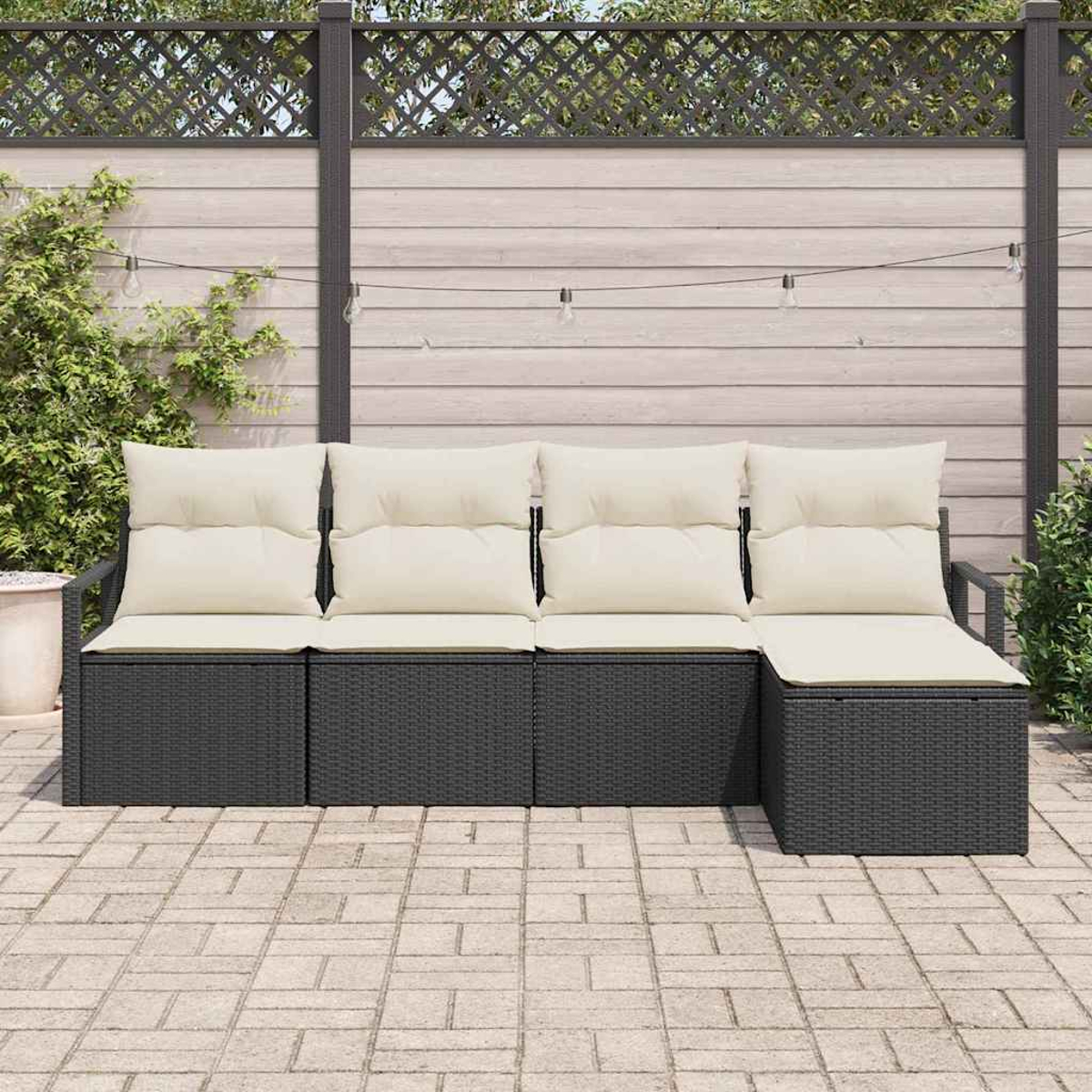 Outdoor-Ecksofa mit cremefarbenen Kissen. Dunkler Korbrahmen, heller Holzzaun im Hintergrund, Lichterkette und Backstein-Patio.