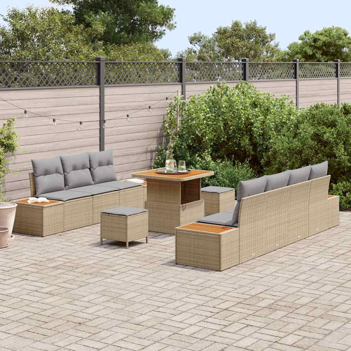 Gartenmöbel-Set mit beigefarbenen Korbsesseln und quadratischem Tisch auf einer Ziegelterrasse, umgeben von Grün und einem Zaun.