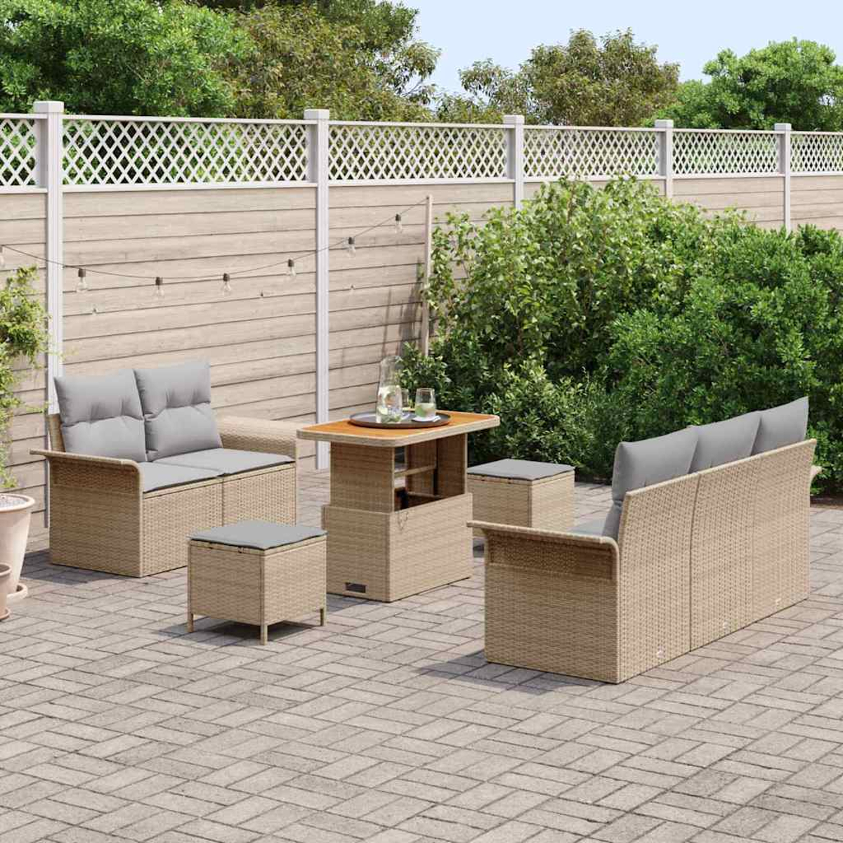 Garten-Terrassenset mit beigen Möbeln, grauen Kissen und einem Holztisch. Ein weißer Gitterzaun und Grünzeug im Hintergrund.