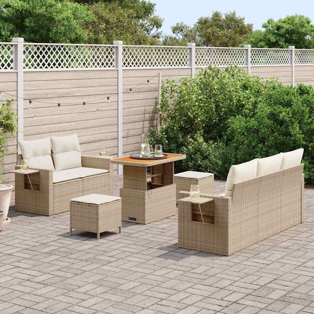Gartenmöbel-Set. Beinhaltet Sofa, Stühle, Tisch und Ottomanen, alles aus beigem Korb. Auf einer Ziegelterrasse mit Zaun im Hintergrund.
