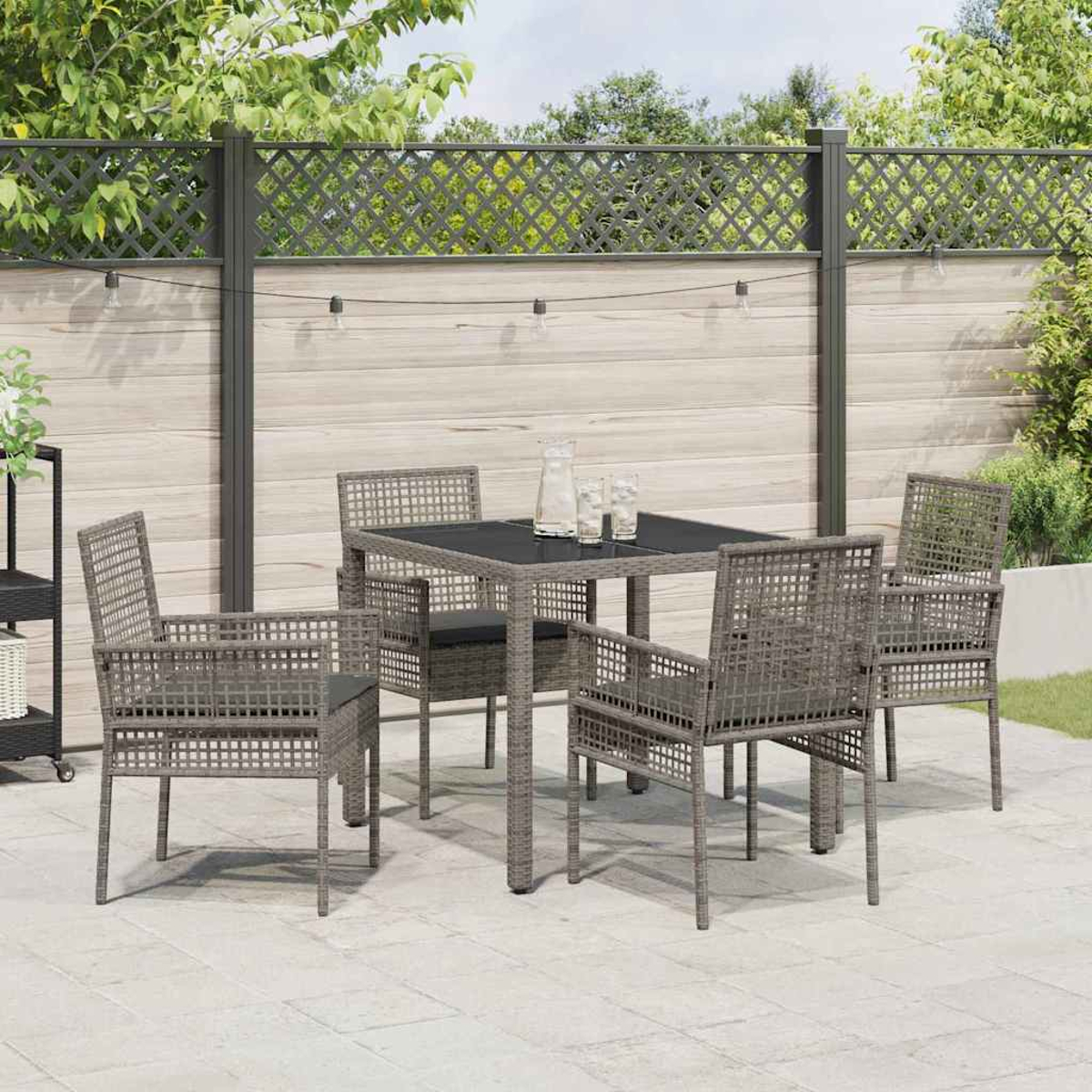 Terrassenset mit grauen Korbstühlen und Tisch. Gläser und ein Krug stehen auf dem Tisch. Im Hintergrund ist ein Holzzaun zu sehen.