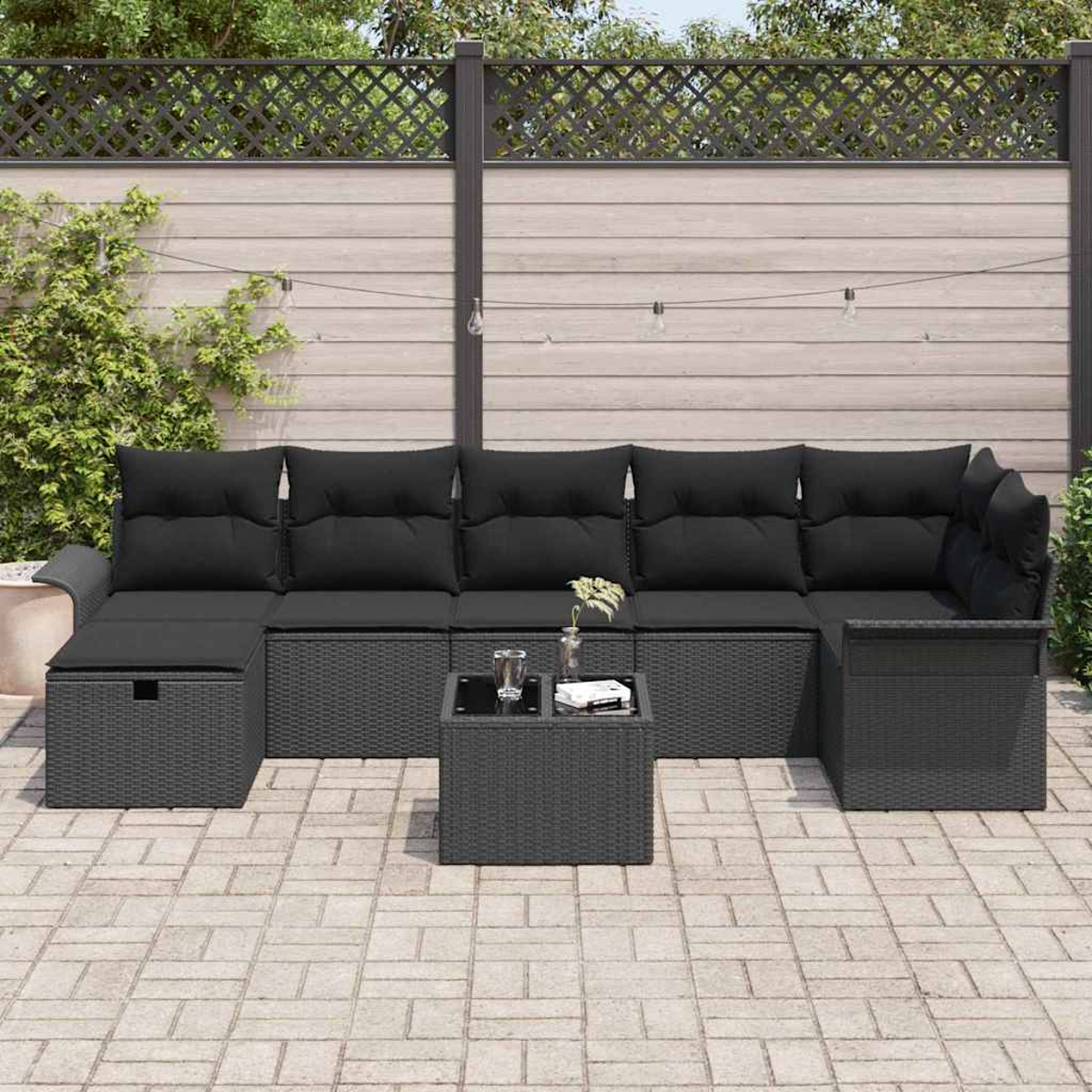 Garten-Terrassenset. Schwarzes gewebtes Sofa und Ottoman mit schwarzen Kissen und einem kleinen Tisch. Auf einer gefliesten Terrasse mit Holzzaun.