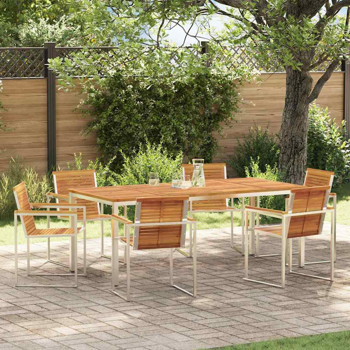 Un juego de mesa y sillas de madera en un patio de ladrillo en un jardín. Arbustos y árboles verdes forman el fondo. Una jarra y vasos están sobre la mesa.
