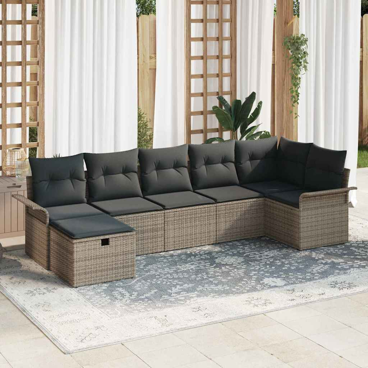 Ein Ecksofa mit grauen Kissen steht auf einem gemusterten Teppich. Weiße Vorhänge und Holzgitter im Hintergrund.