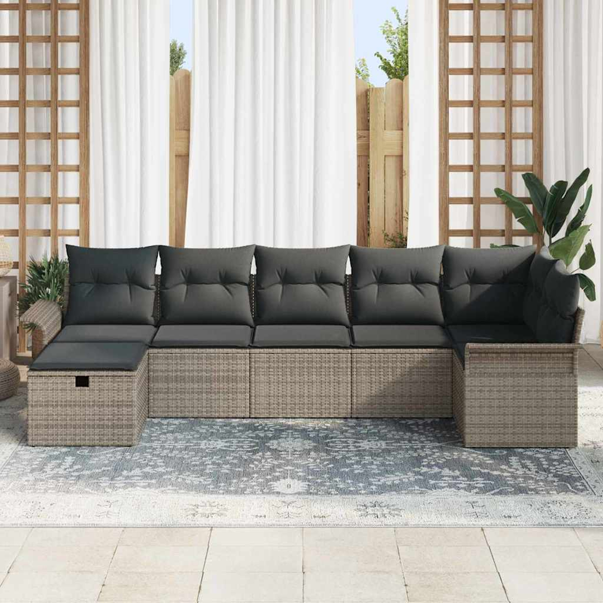 Outdoor-Ecksofa mit dunkelgrauen Kissen auf einem gemusterten Teppich. Weiße Vorhänge und Holzgitter im Hintergrund.
