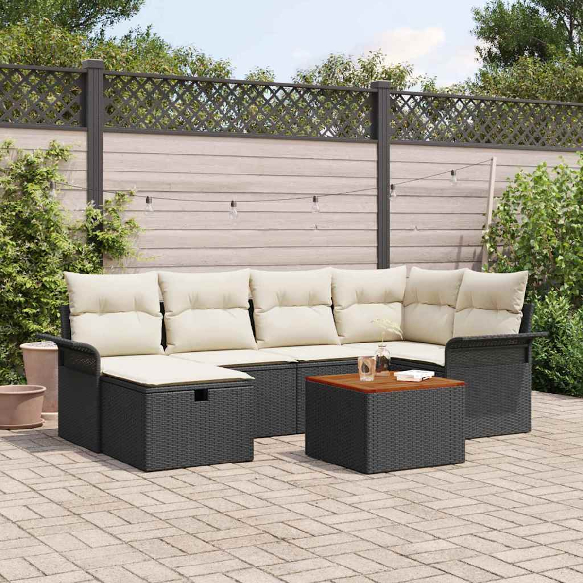 Terrassenmöbel-Set mit grau gewebten Möbeln und cremefarbenen Kissen. Enthält einen Couchtisch. Im Hintergrund sind ein Zaun und Grün.