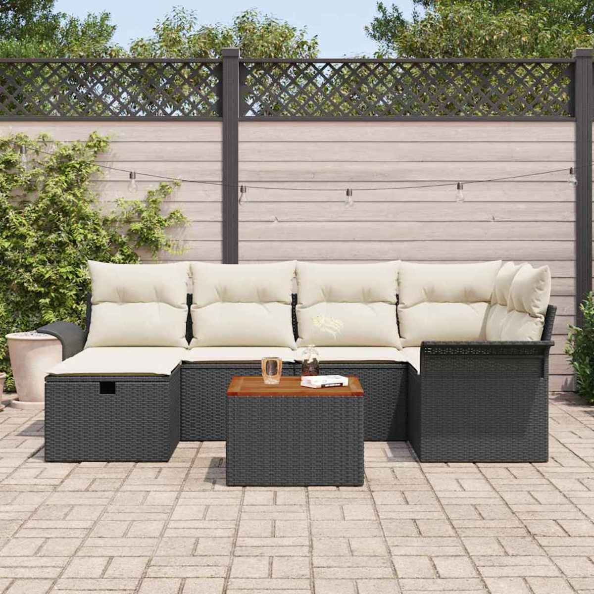 Gartenmöbel: graues Korbmöbel mit cremefarbenen Kissen und einem kleinen Tisch, auf einer gepflasterten Terrasse mit Zaun als Hintergrund.
