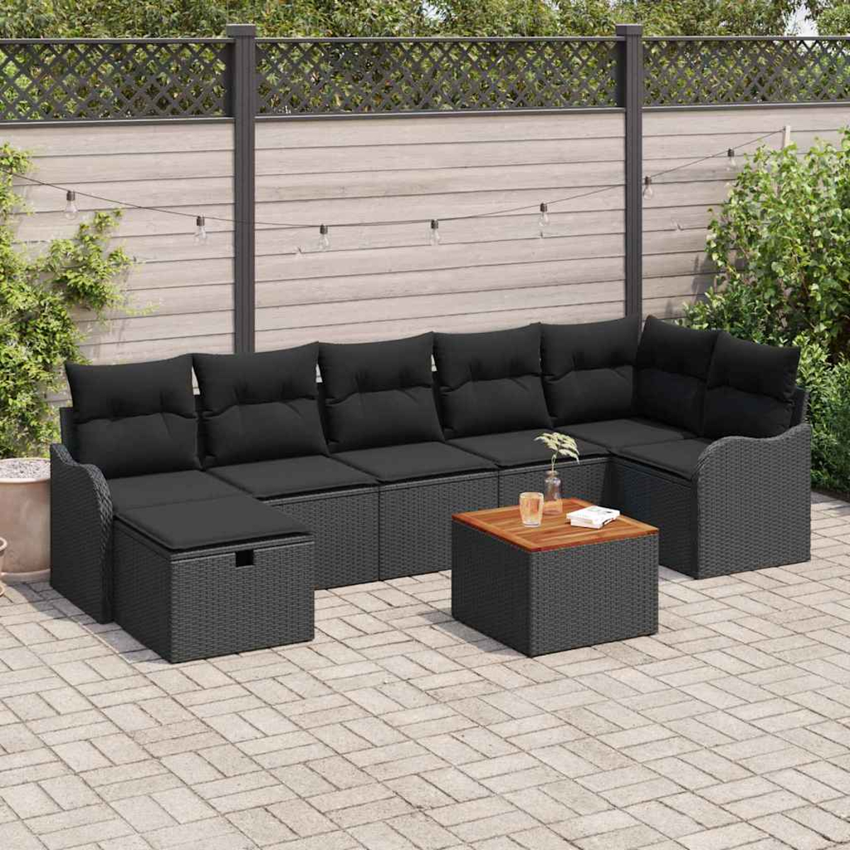Outdoor-Ecksofa mit schwarzen Kissen und einem Holztisch. Auf einer gepflasterten Terrasse mit Holzzaun im Hintergrund.