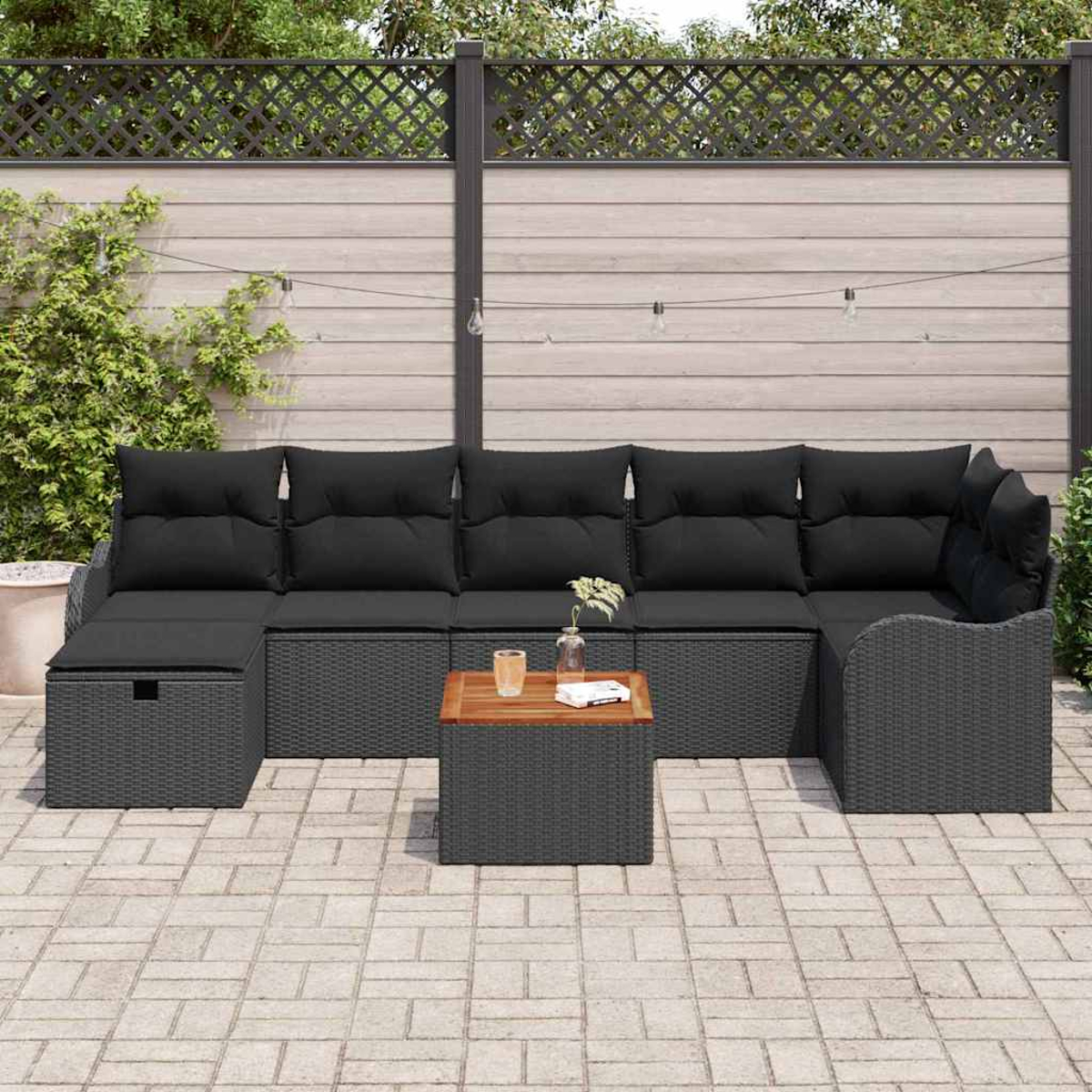 Außenszene mit einem grauen Korbsessel und einem kleinen Holztisch. Schwarze Kissen und eine gepflasterte Terrasse sind sichtbar.