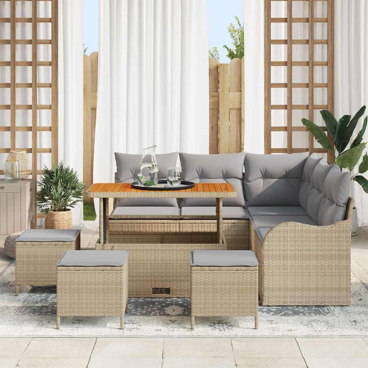 Gartenmöbel-Set aus Rattan mit grauen Kissen, einem Tisch mit Glaskrug und drei Hockern. Der Hintergrund umfasst weiße Vorhänge.