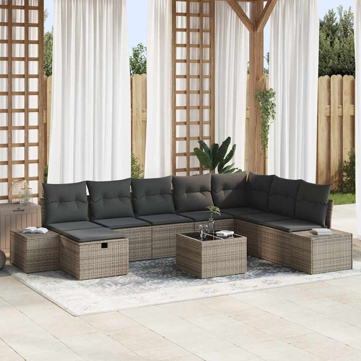 Ein Outdoor-Ecksofa mit grauen Kissen und einem Couchtisch steht auf einem Teppich. Im Hintergrund befinden sich weiße Vorhänge und Holzbalken.