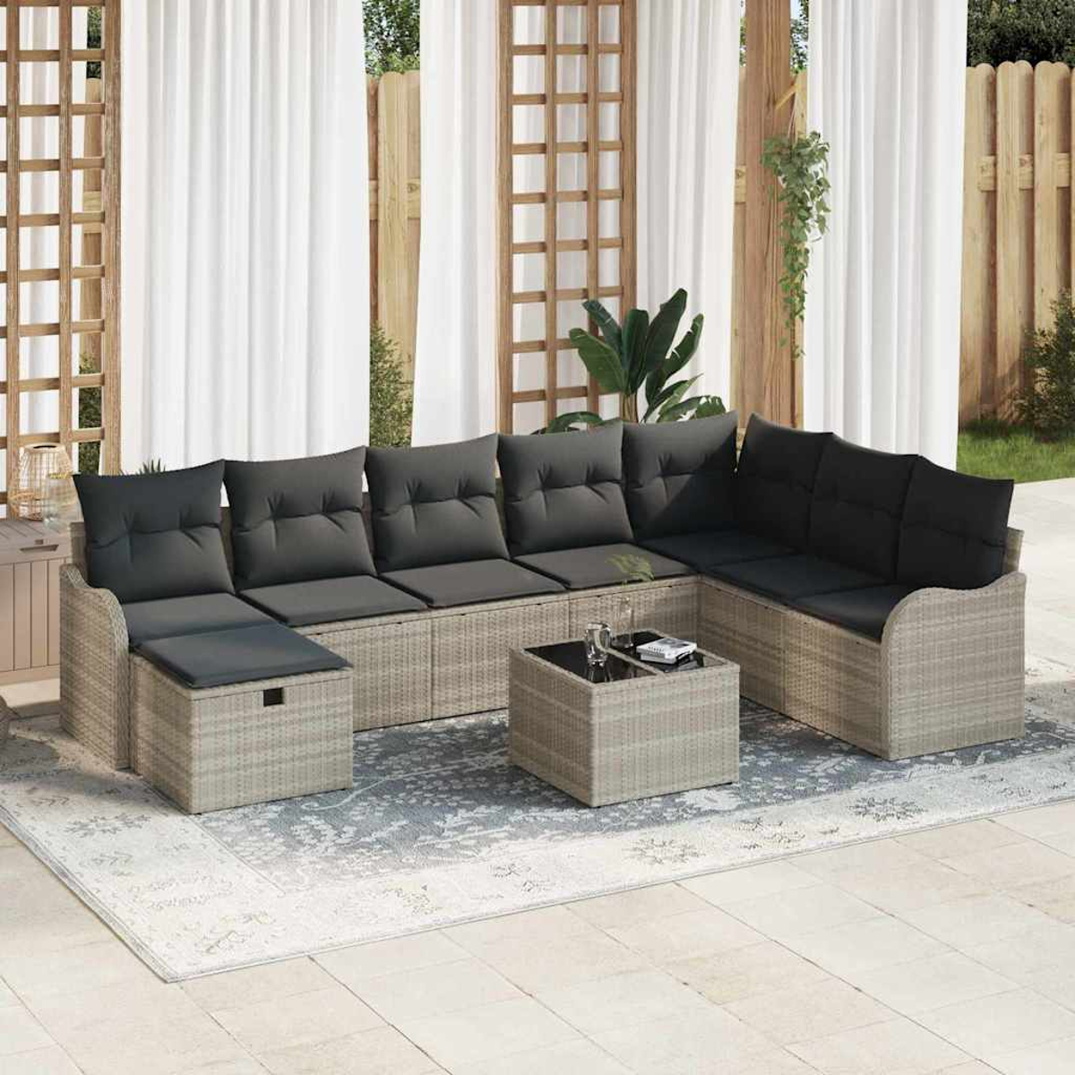 Ein graues Outdoor-Ecksofa mit schwarzen Kissen, ein quadratischer Tisch und ein Teppich befinden sich auf einer Terrasse. Weiße Vorhänge und Holzgitter im Hintergrund.