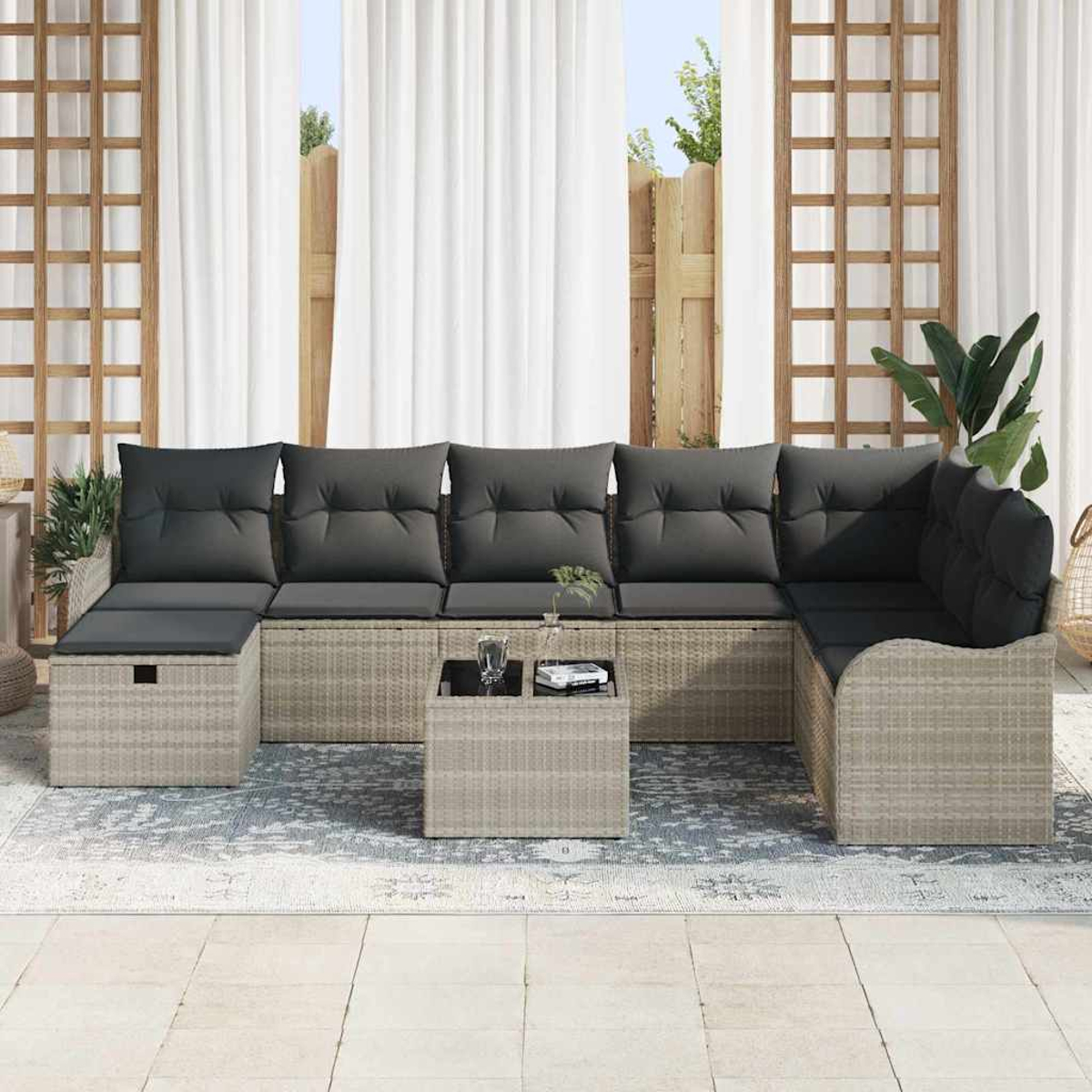 Ein Outdoor-Ecksofa mit grauen Kissen. Ein kleiner Tisch mit Glas und Buch. Weiße Vorhänge und Holzgitter im Hintergrund.