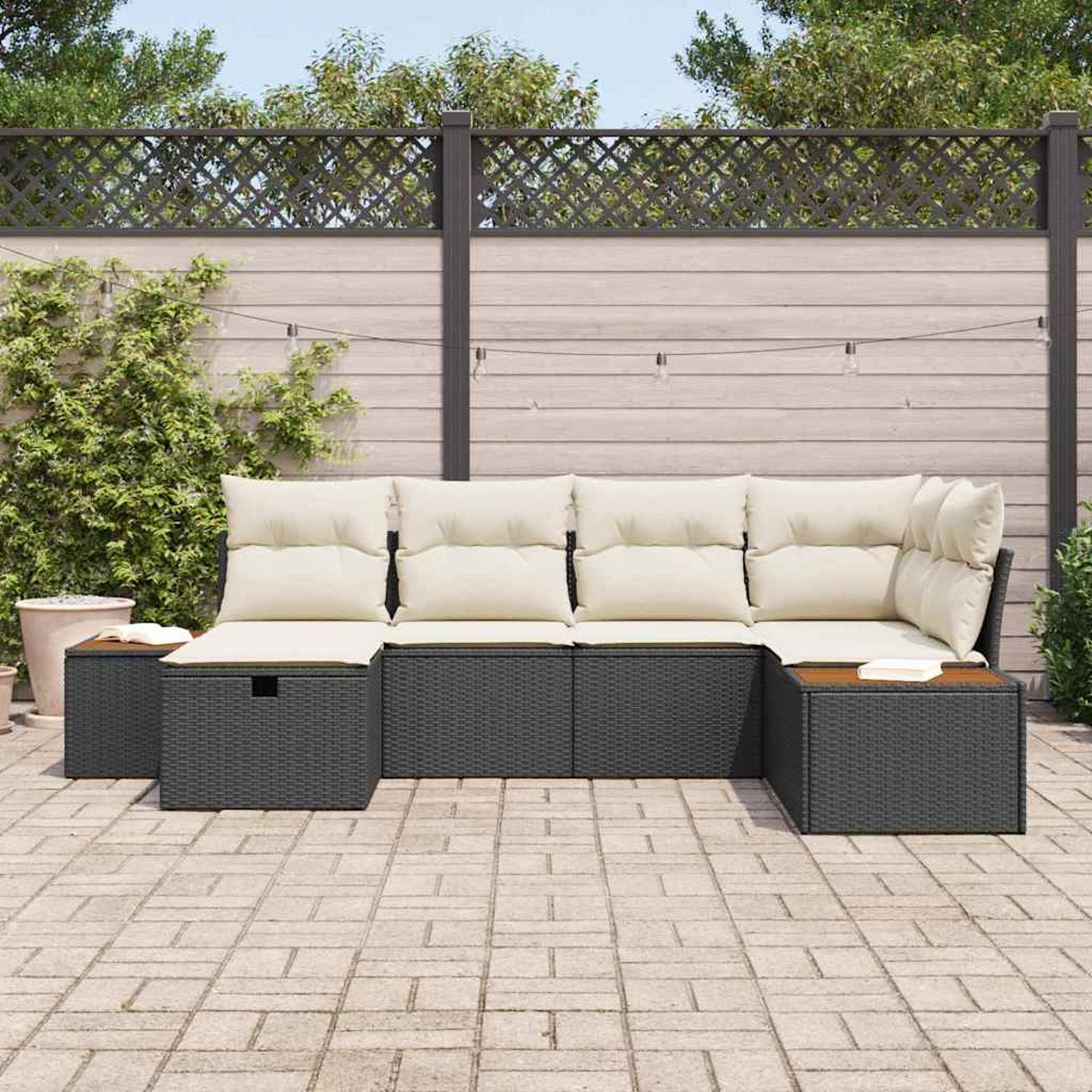 Outdoor-Ecksofa mit cremefarbenen Kissen. Dunkelgrauer Korbrahmen. Beistelltische aus Holz. Terrasse mit Ziegelpflaster und Holzzaun im Hintergrund.