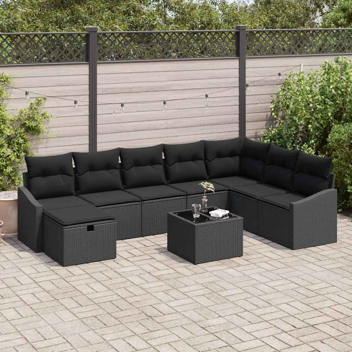 Outdoor-Ecksofa mit schwarzen Kissen. Ein kleiner Tisch mit Gläsern steht auf der Terrasse. Der Hintergrund umfasst einen Zaun und Grün.