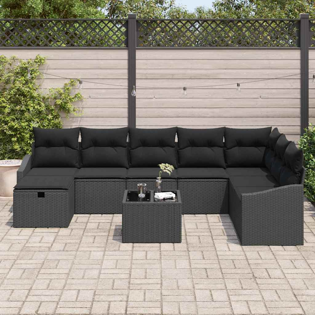 Ein graues Gartensofa mit schwarzen Kissen und einem kleinen Tisch auf einer Steinterrasse. Im Hintergrund ist ein Holzzaun.