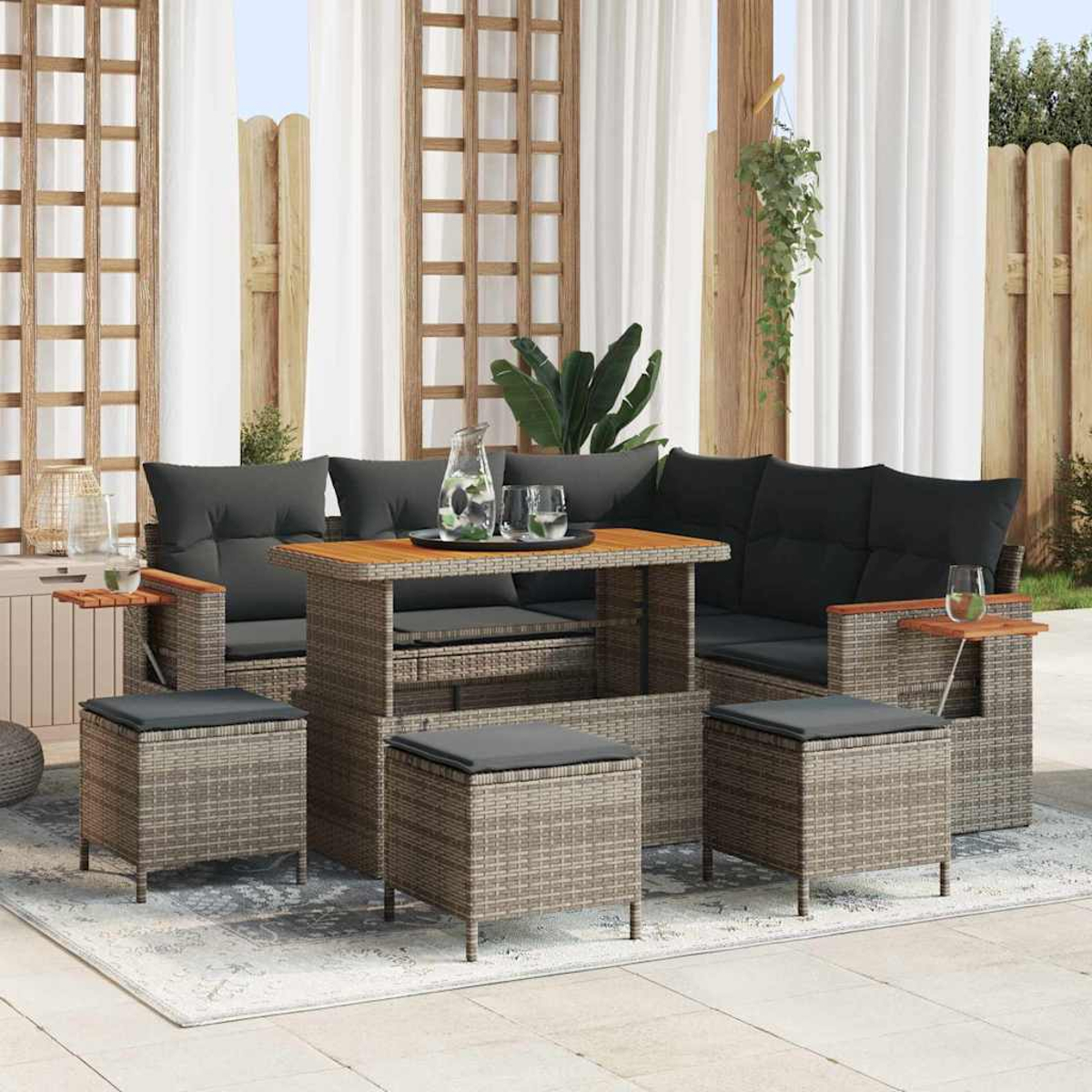 Garten-Terrassenset mit grauem Korbmöbel-Sofa, Tisch und Ottomanen. Schwarze Kissen, Holzakzente und eine Kanne mit Gläsern auf dem Tisch.