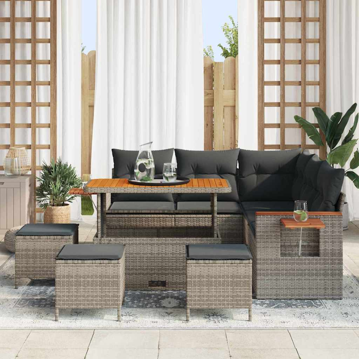 Outdoor-Geflechtmöbel-Set mit grauen Kissen, einem Holztisch und Hockern, vor dem Hintergrund von Vorhängen und einem Zaun.