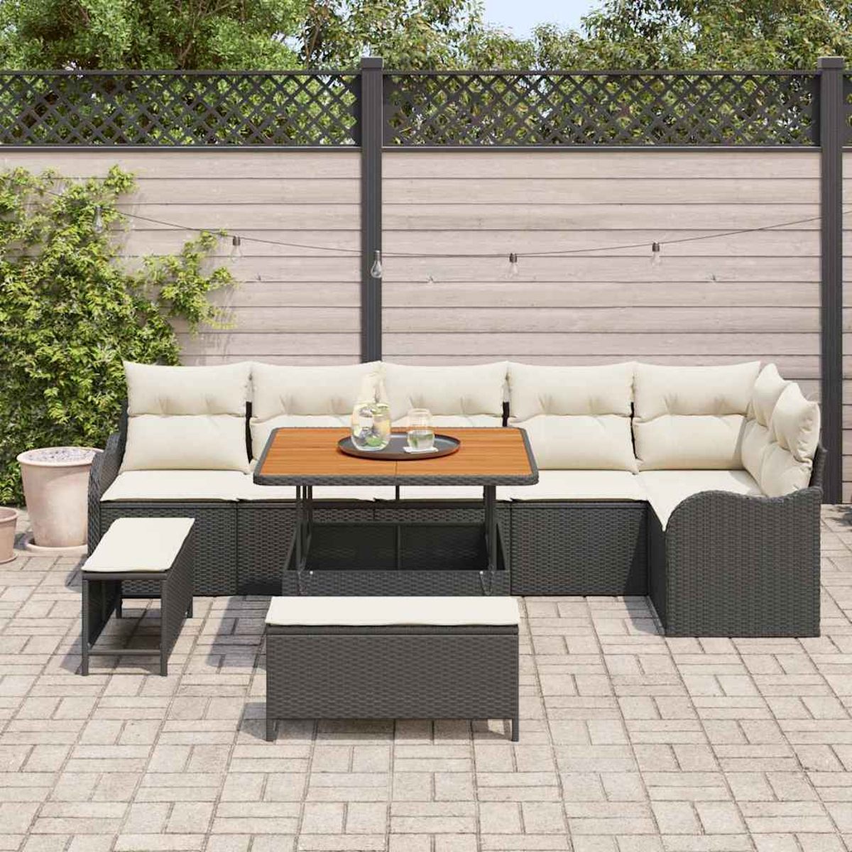Outdoor-Ecksofa mit Kissen, ein Couchtisch mit Getränken und zwei Ottomanen auf einer Backsteinterrasse, umgeben von einem Zaun.