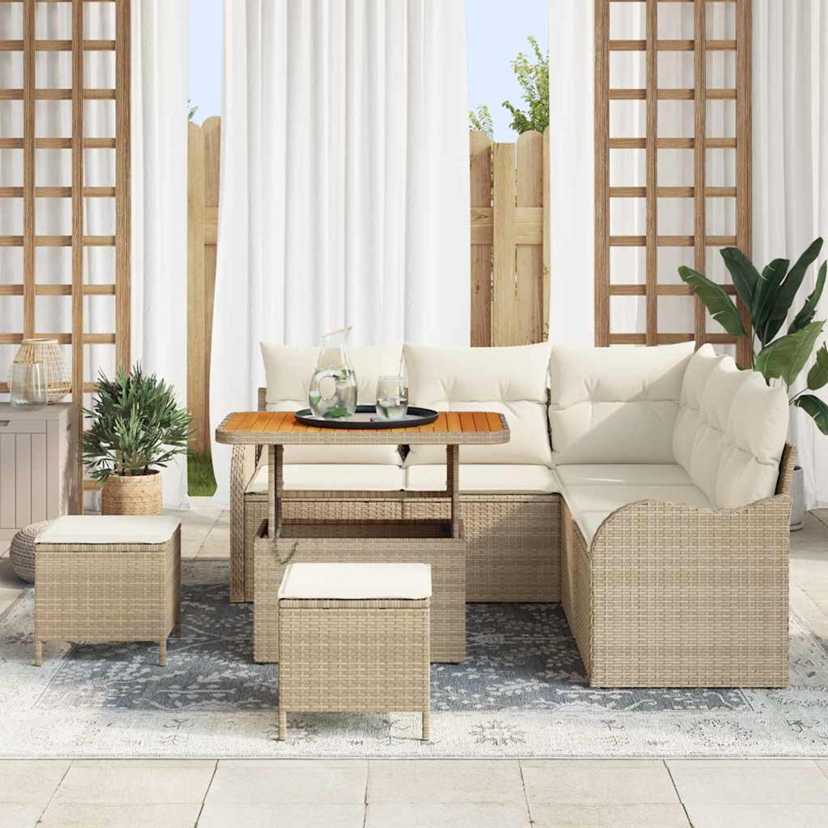 Set di sedute per esterni con mobili beige intrecciati, cuscini bianchi e un tavolo di legno. Include due pouf, una pianta e tende bianche.