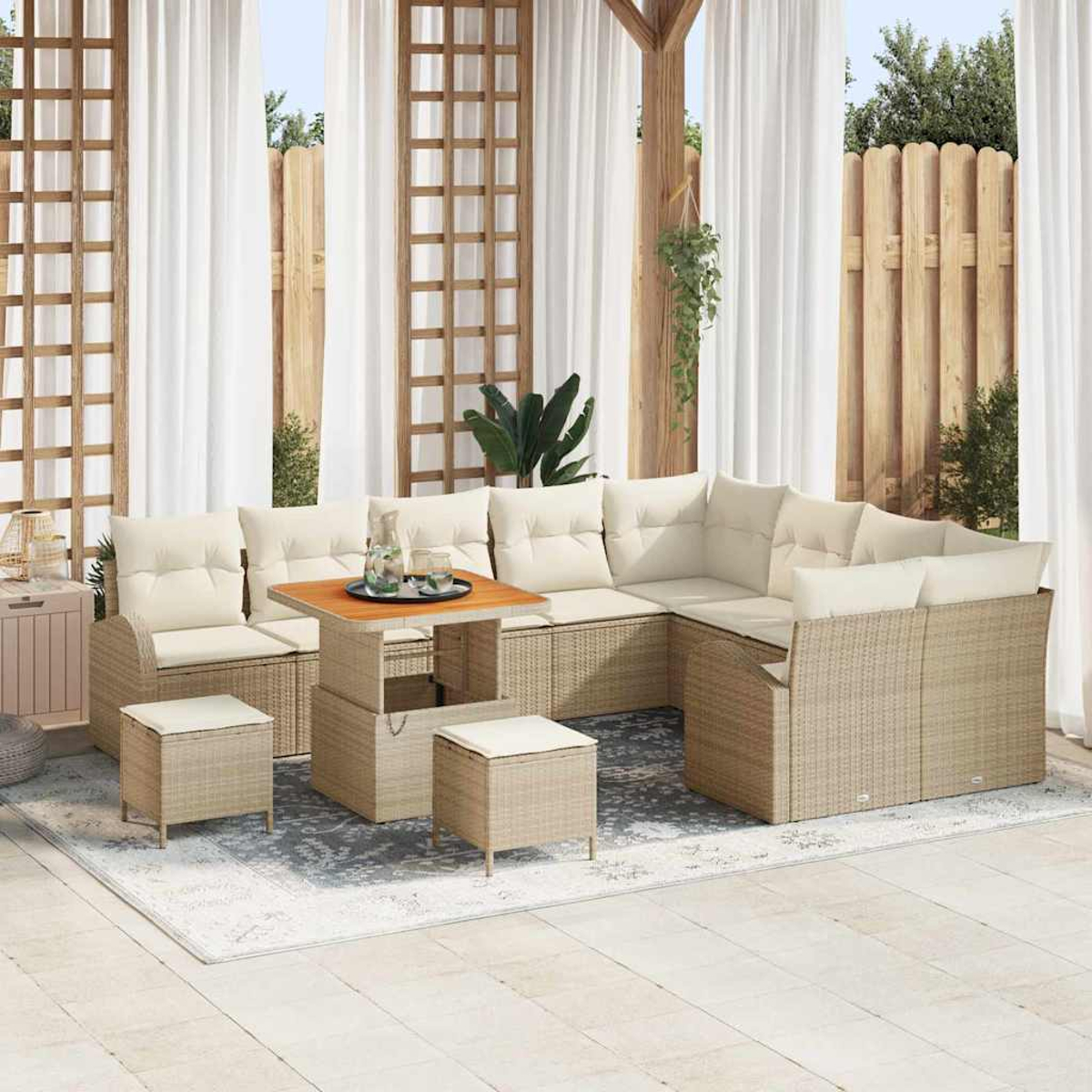Outdoor-Wicker-Möbel-Set mit beigen Kissen. Enthält Sofa, Tisch und Hocker. Auf einem gemusterten Teppich, mit Vorhängen im Hintergrund.